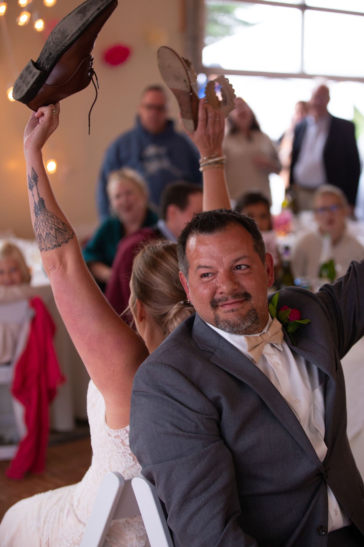 Wedding couple holding up shoes during reception game at decorated venue.