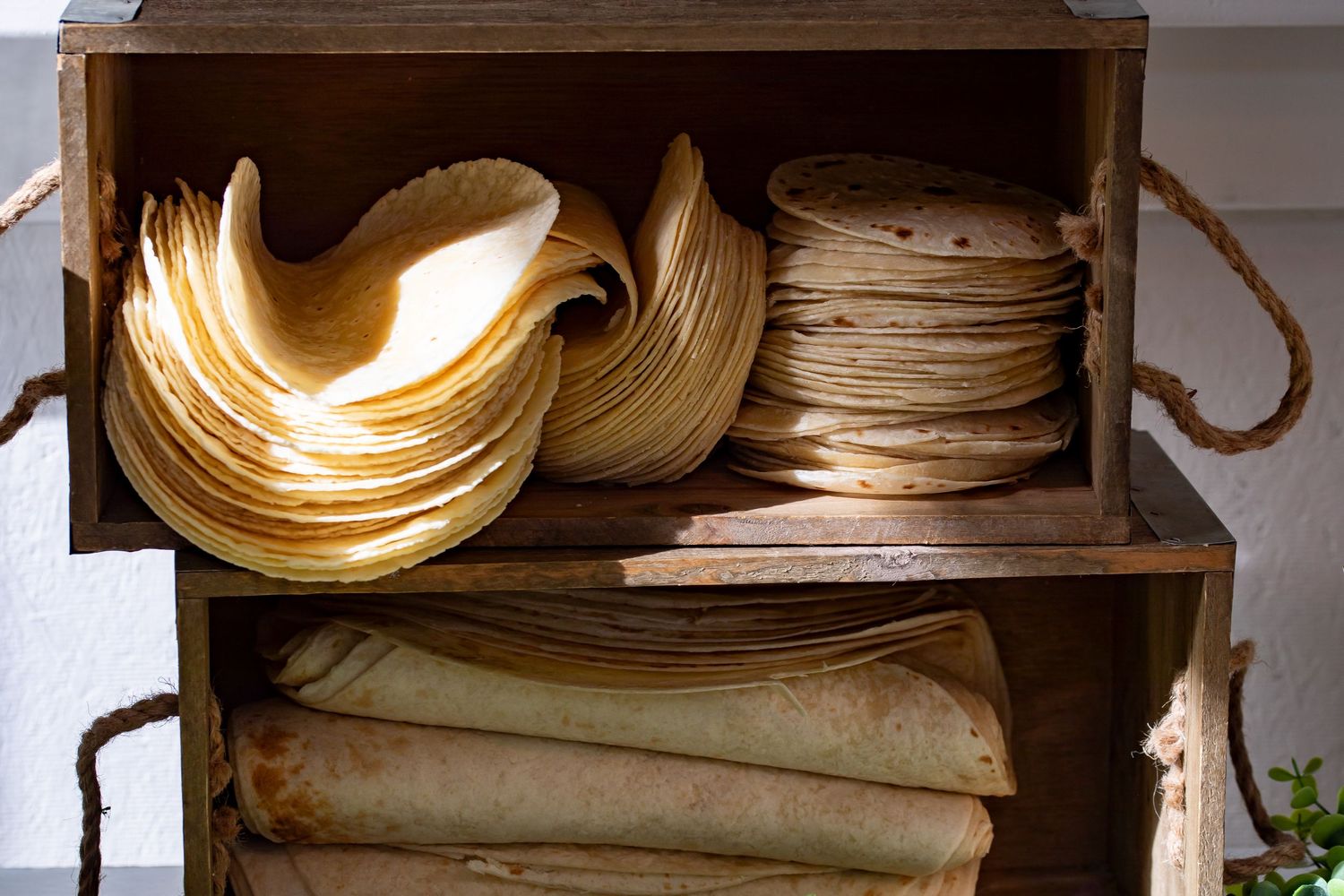 Wooden crates filled with stacked vintage plates and linens with rope handles.