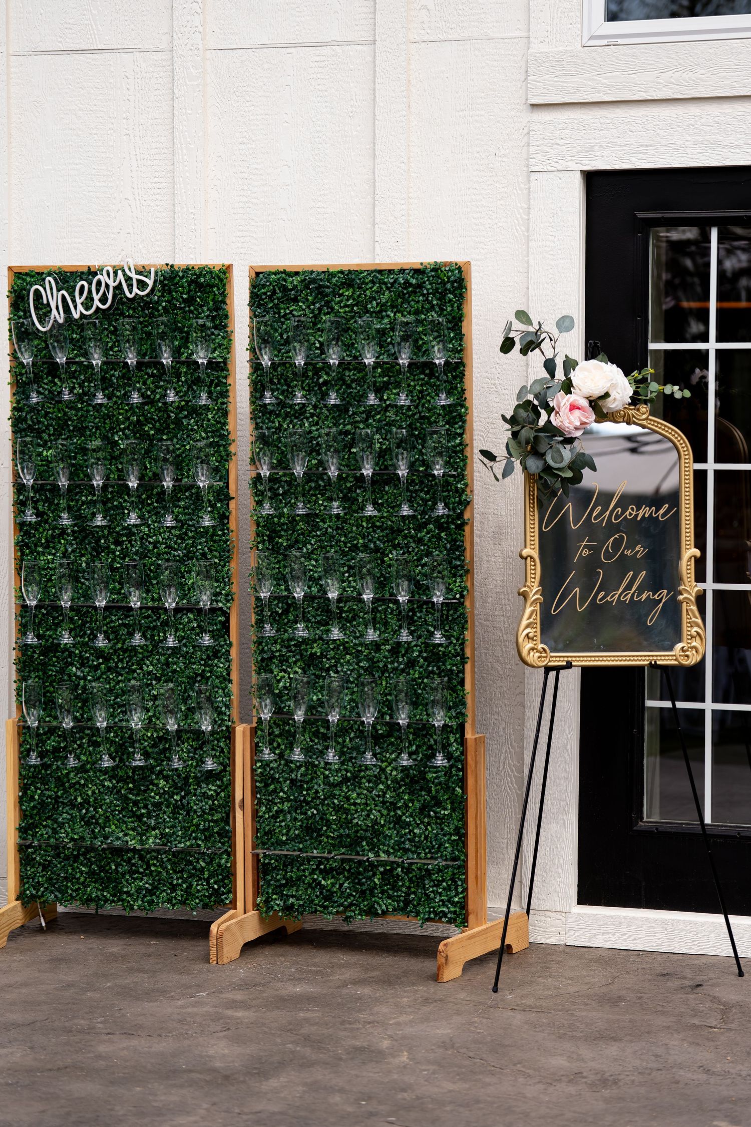 Wedding decor featuring artificial green hedge walls and a welcome sign with gold frame.