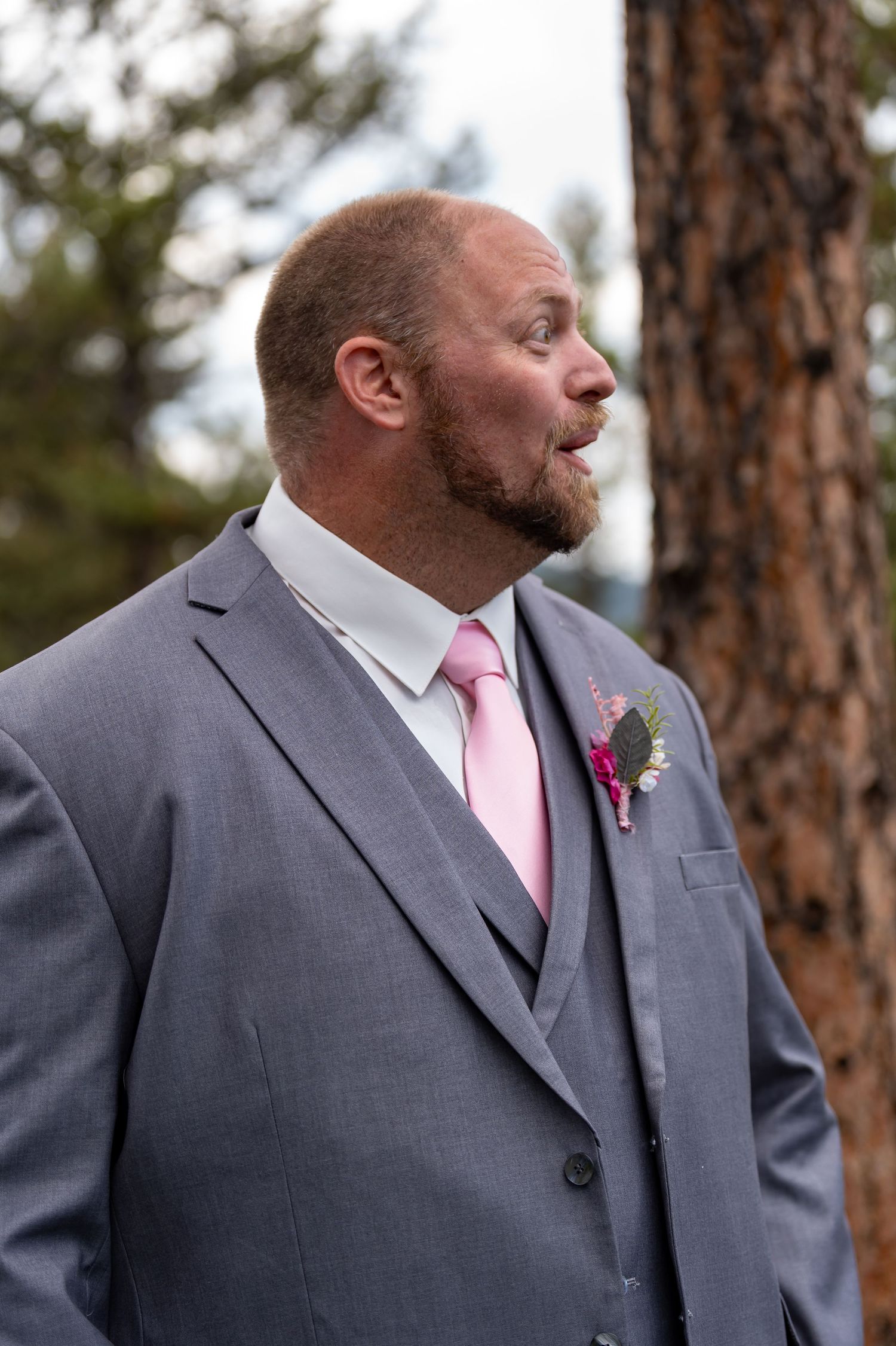 Groomsman in grey suit with pink tie looking to the side during ceremony.