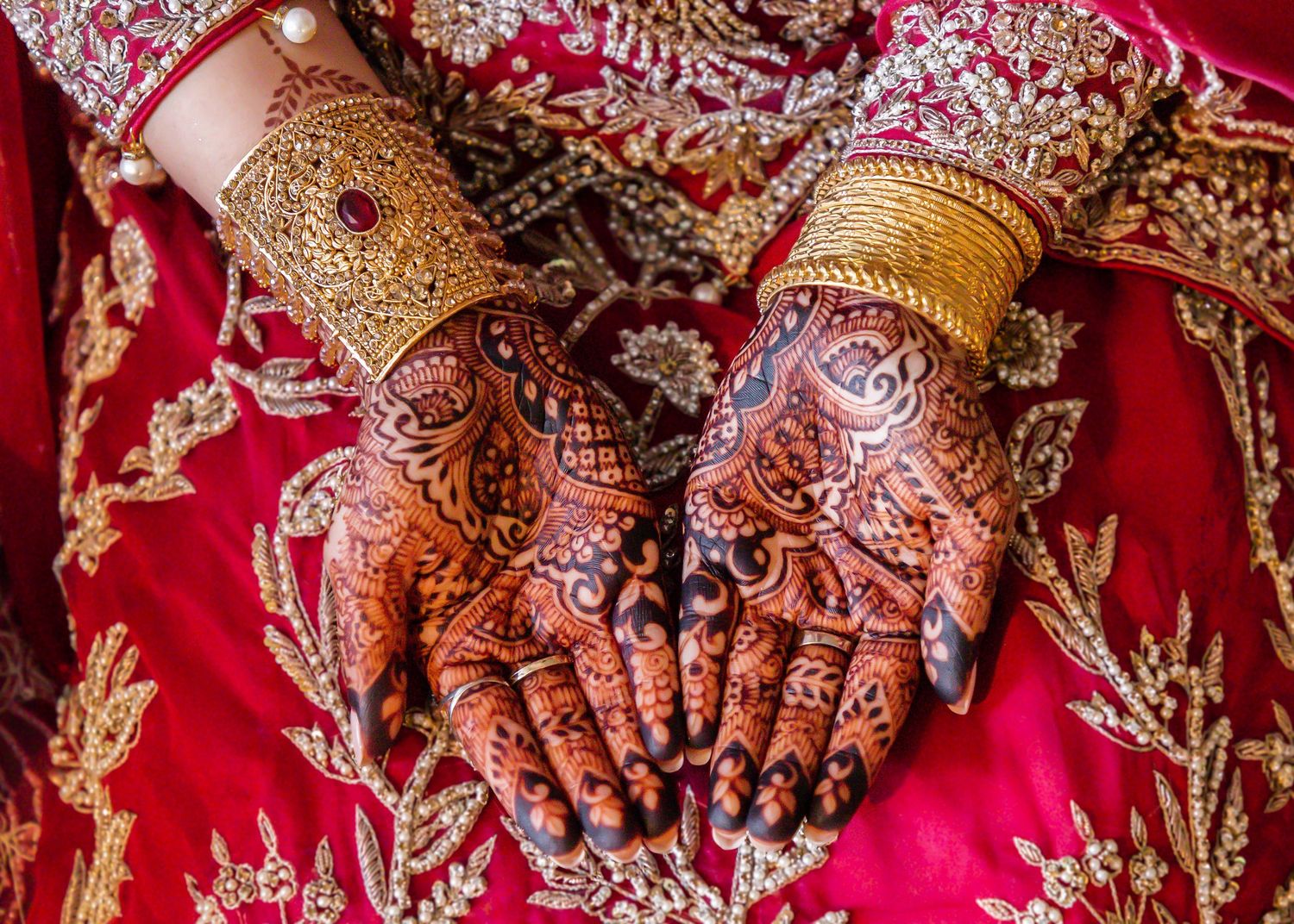 Intricate henna designs adorned with gold bangles on traditional bridal hands.