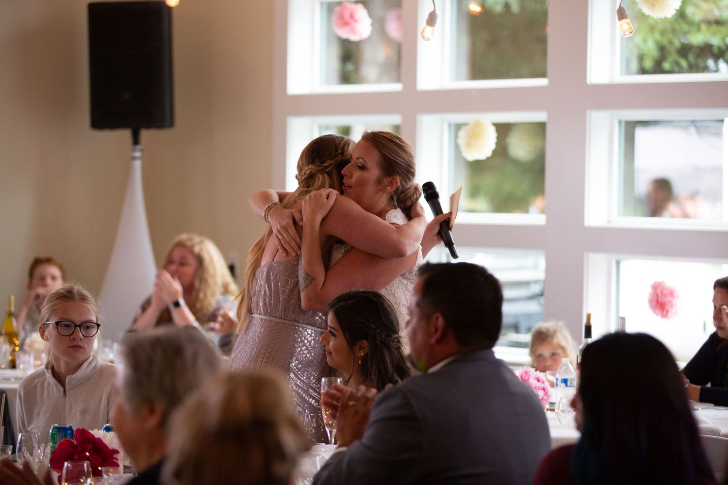 Wedding reception guests celebrating and dancing in a bright windowed venue.