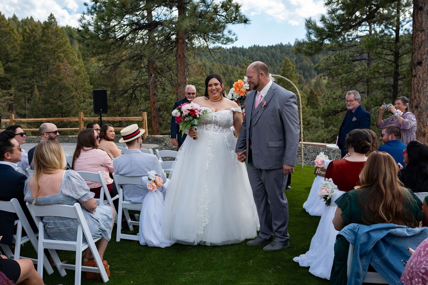 An outdoor wedding ceremony setup with white chairs and forest scenery in the background.