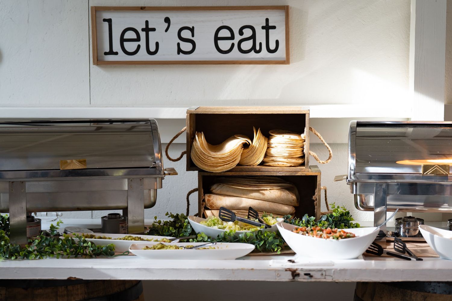 Buffet setup with chafing dishes and 'Let's Eat' sign displayed above serving station.