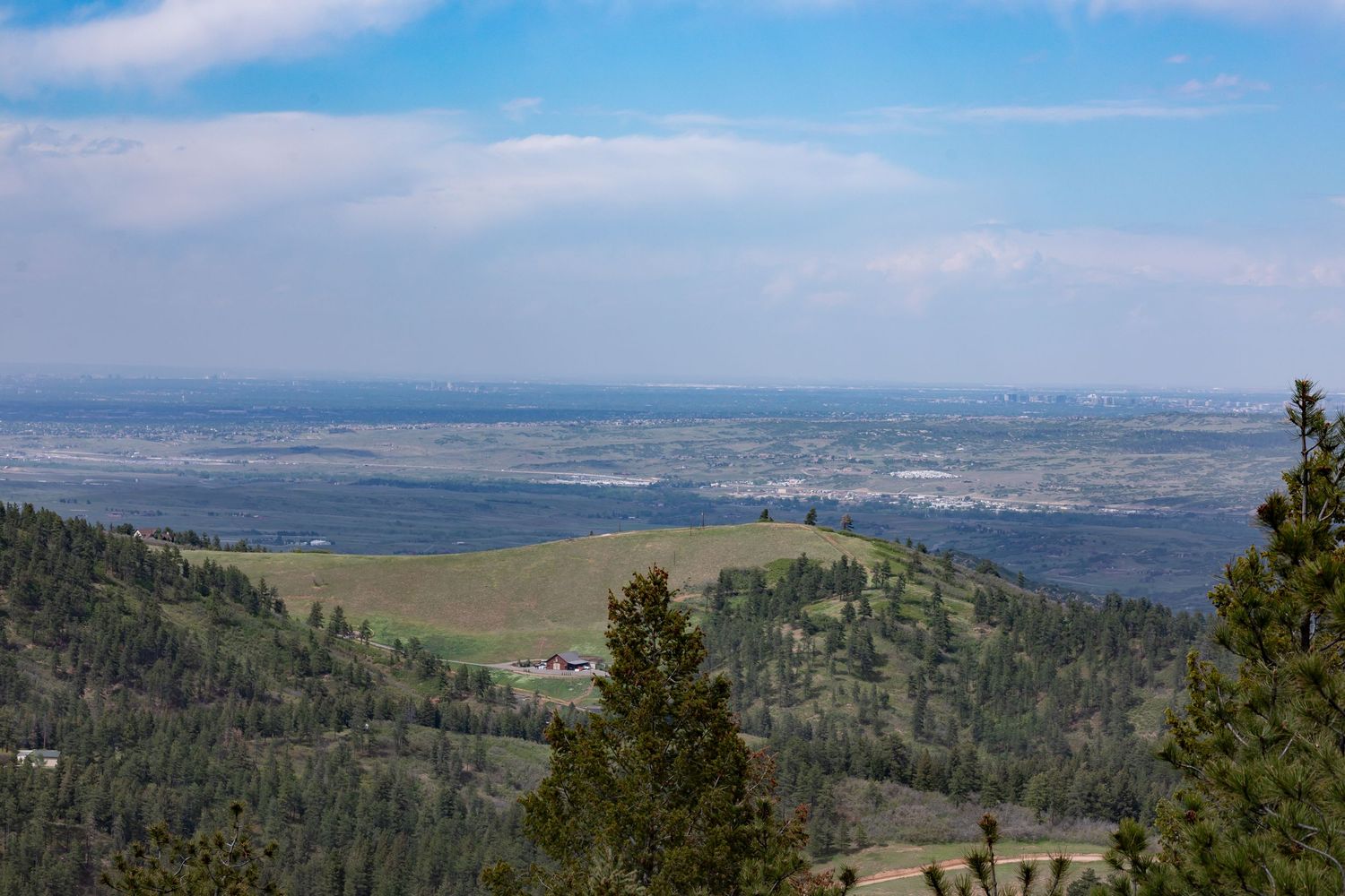 Panoramic valley view from mountaintop showing distant city and pine forest.