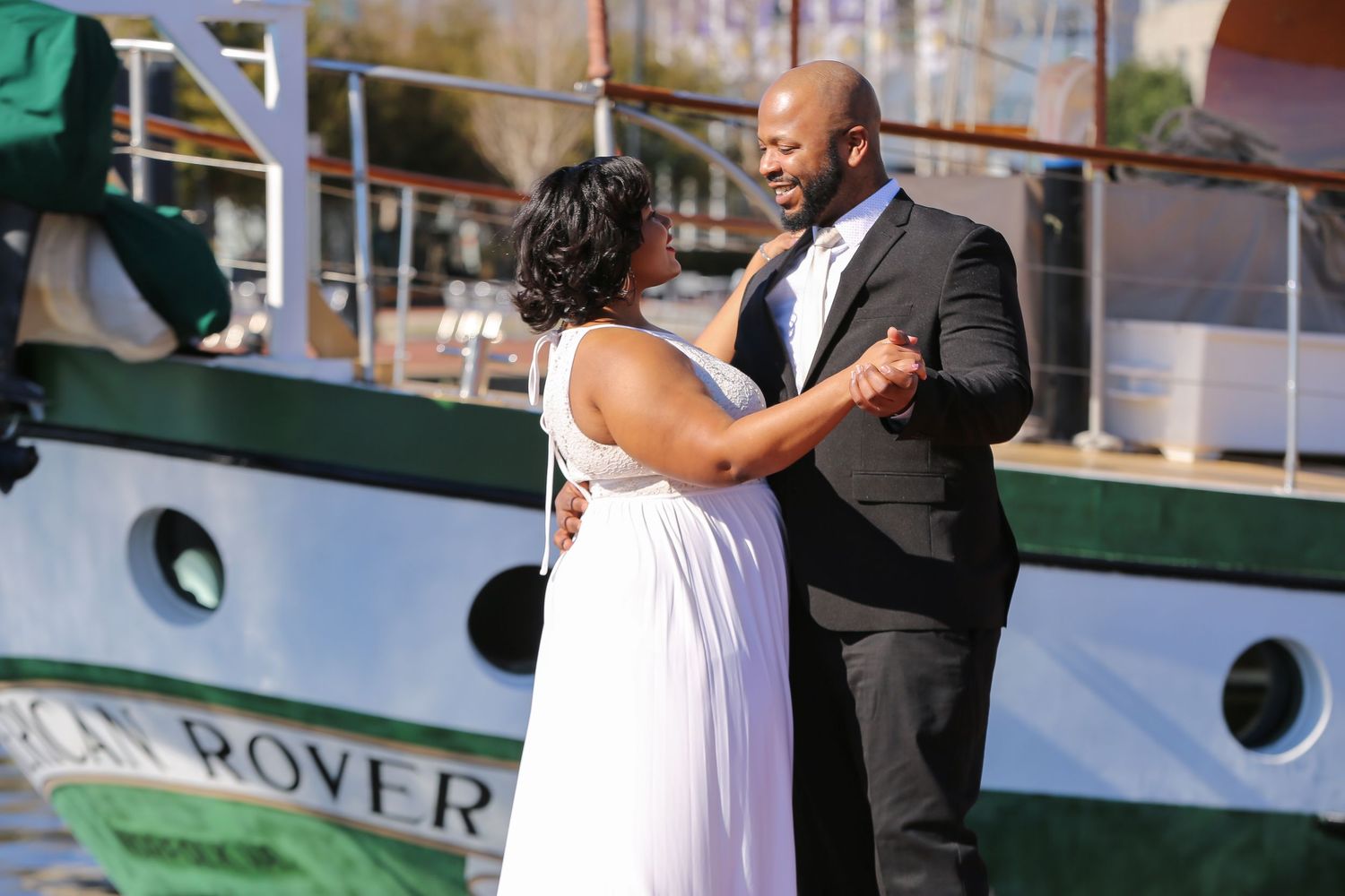 A couple dances together on a cruise ship deck with the ocean and blue sky visible in the background.