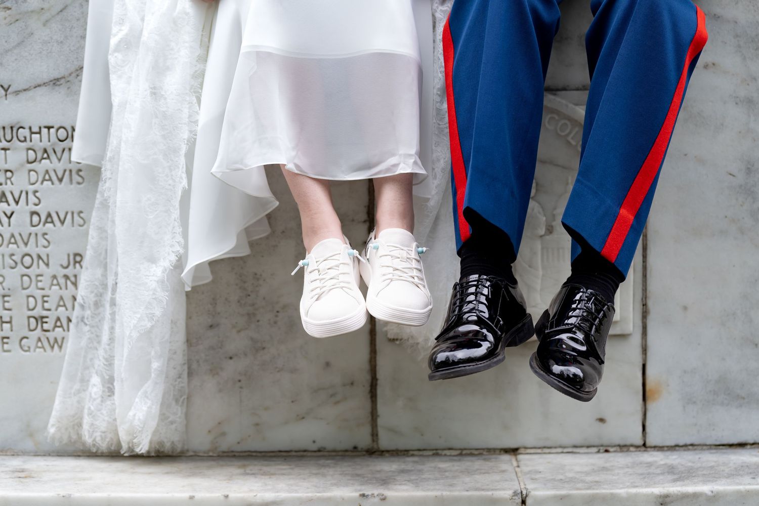 Wedding couple's feet dangling from marble ledge showing dress shoes and sneakers.