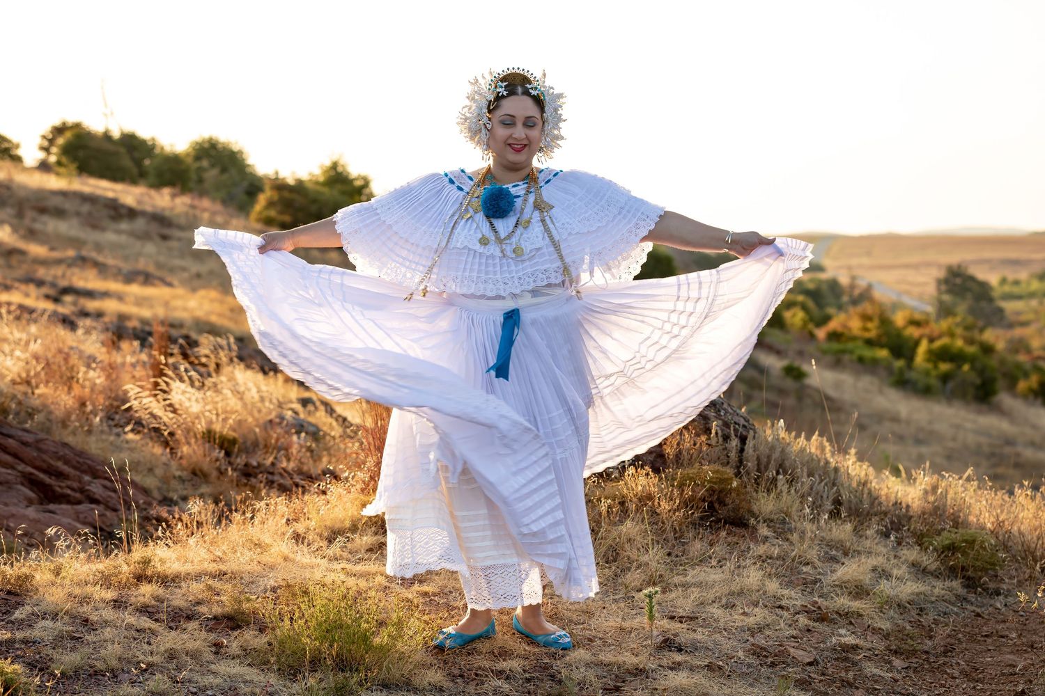 A dancer in a flowing white dress with floral headpiece twirls gracefully against a golden sunset landscape.