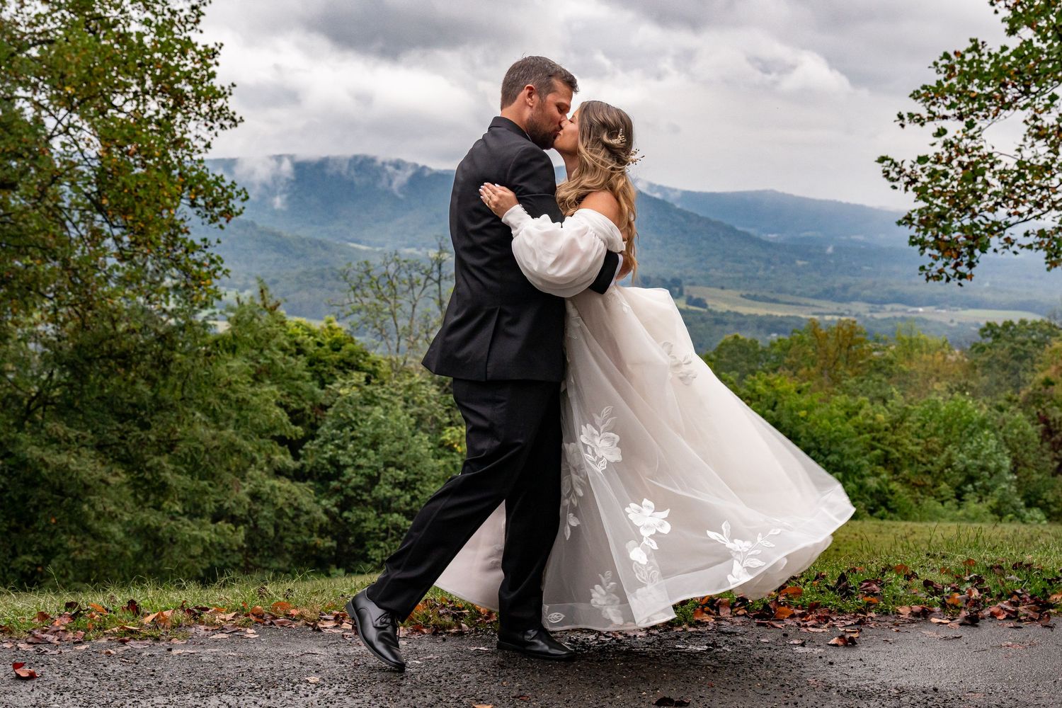 Wedding couple poses with mountain landscape and cloudy sky in background.
