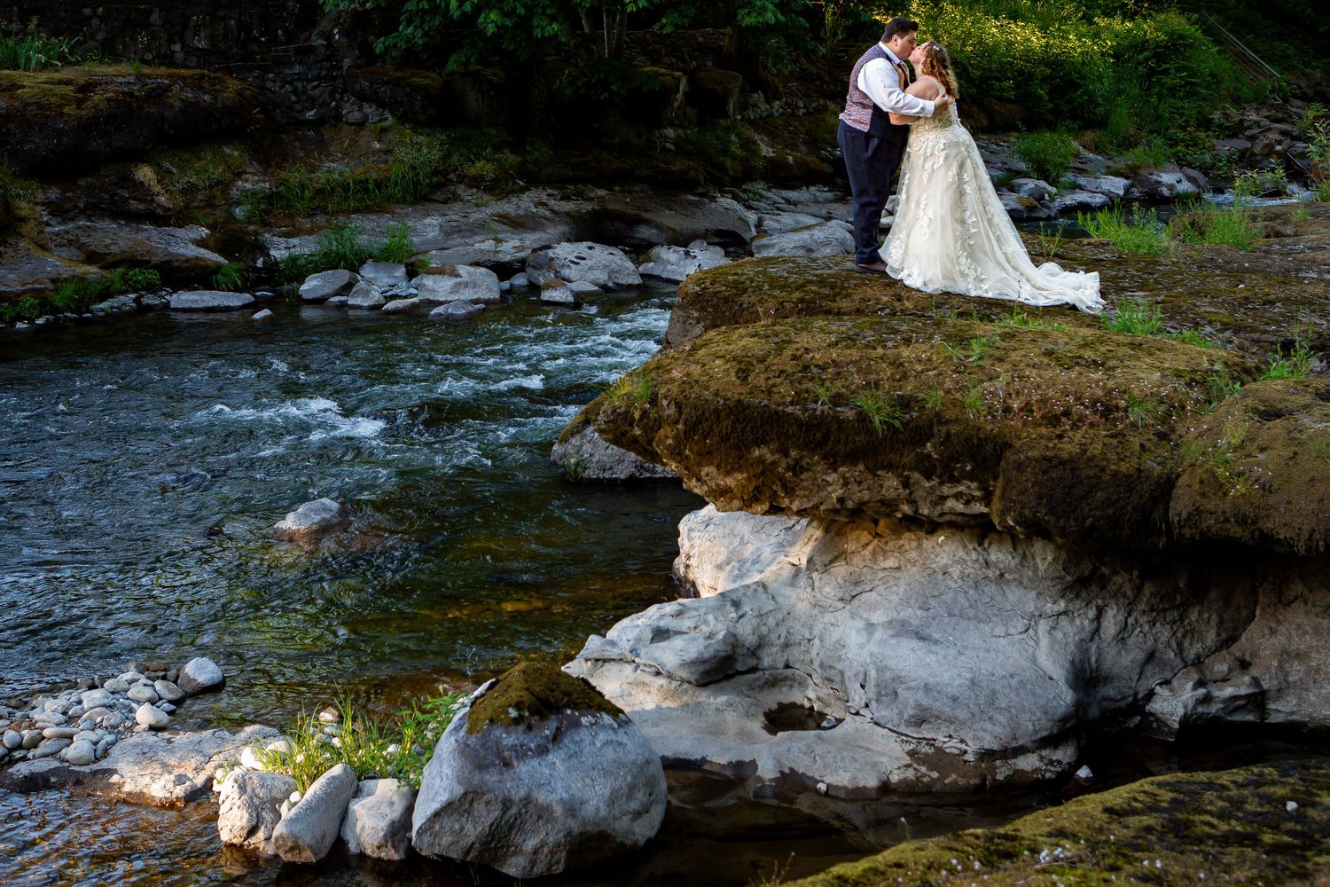 A romantic wedding portrait against a rocky riverbank in a forest setting.