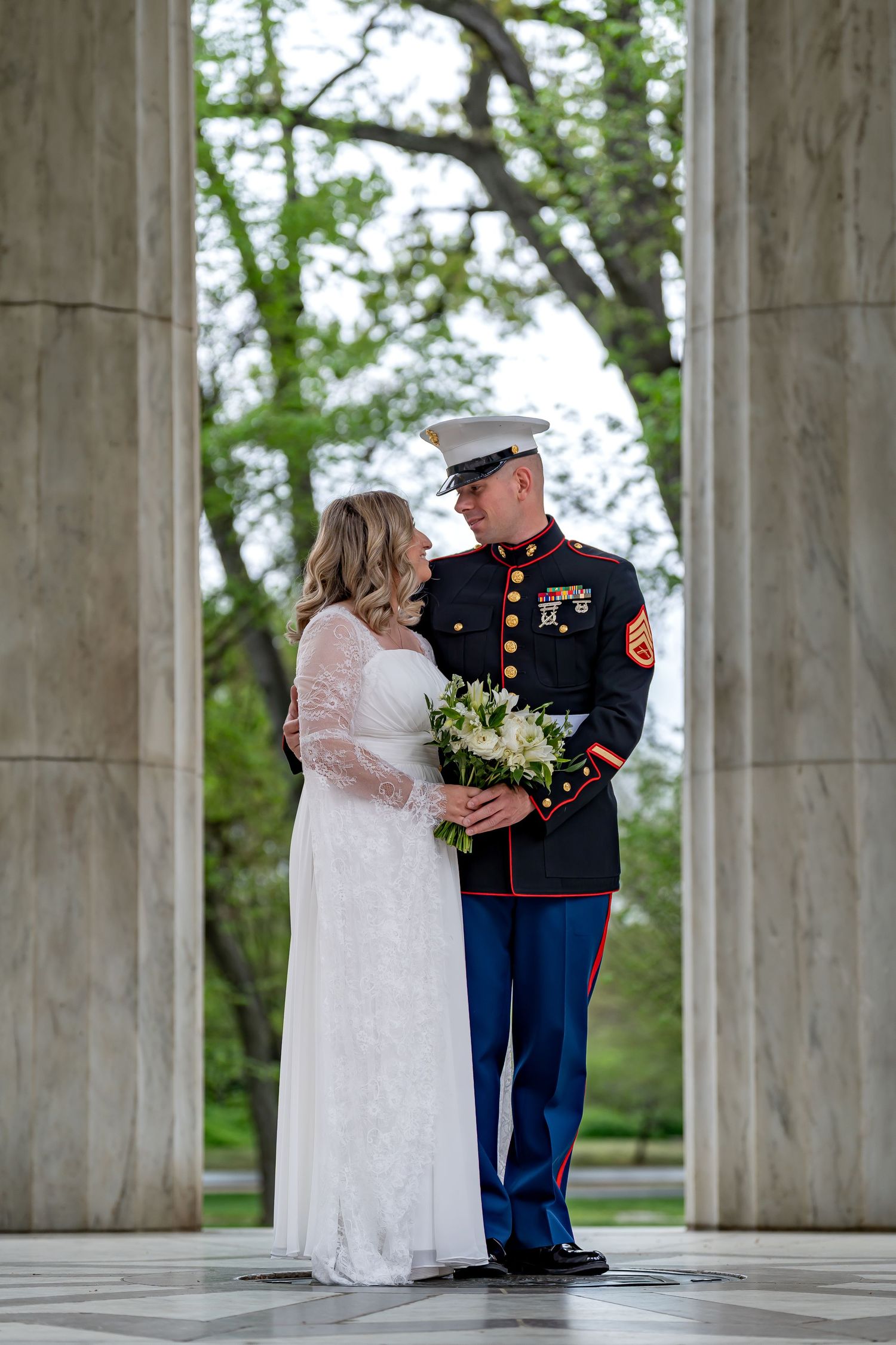 Military wedding portrait of couple standing between classical columns in formal attire.