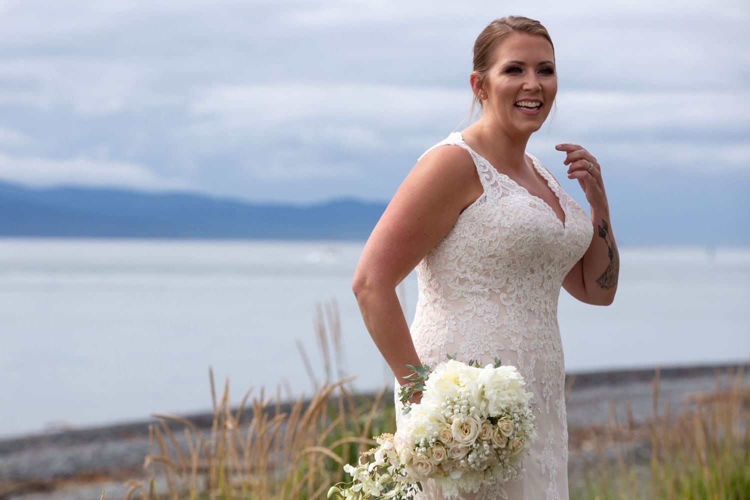 A scenic wedding photoshoot on a coastal beach with someone in a white dress holding a bouquet of white flowers.