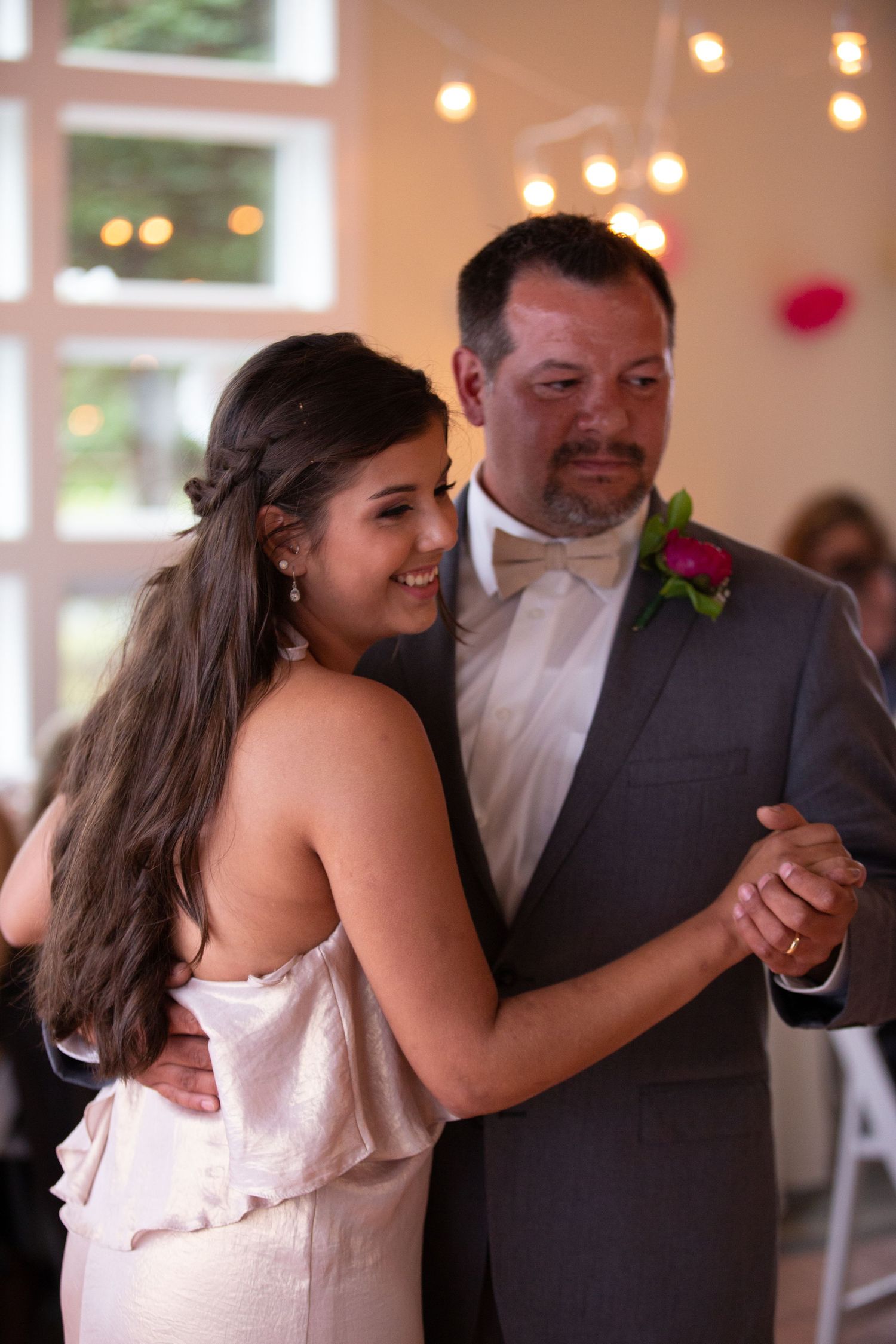 A joyful father-daughter dance at a wedding reception with twinkling lights.