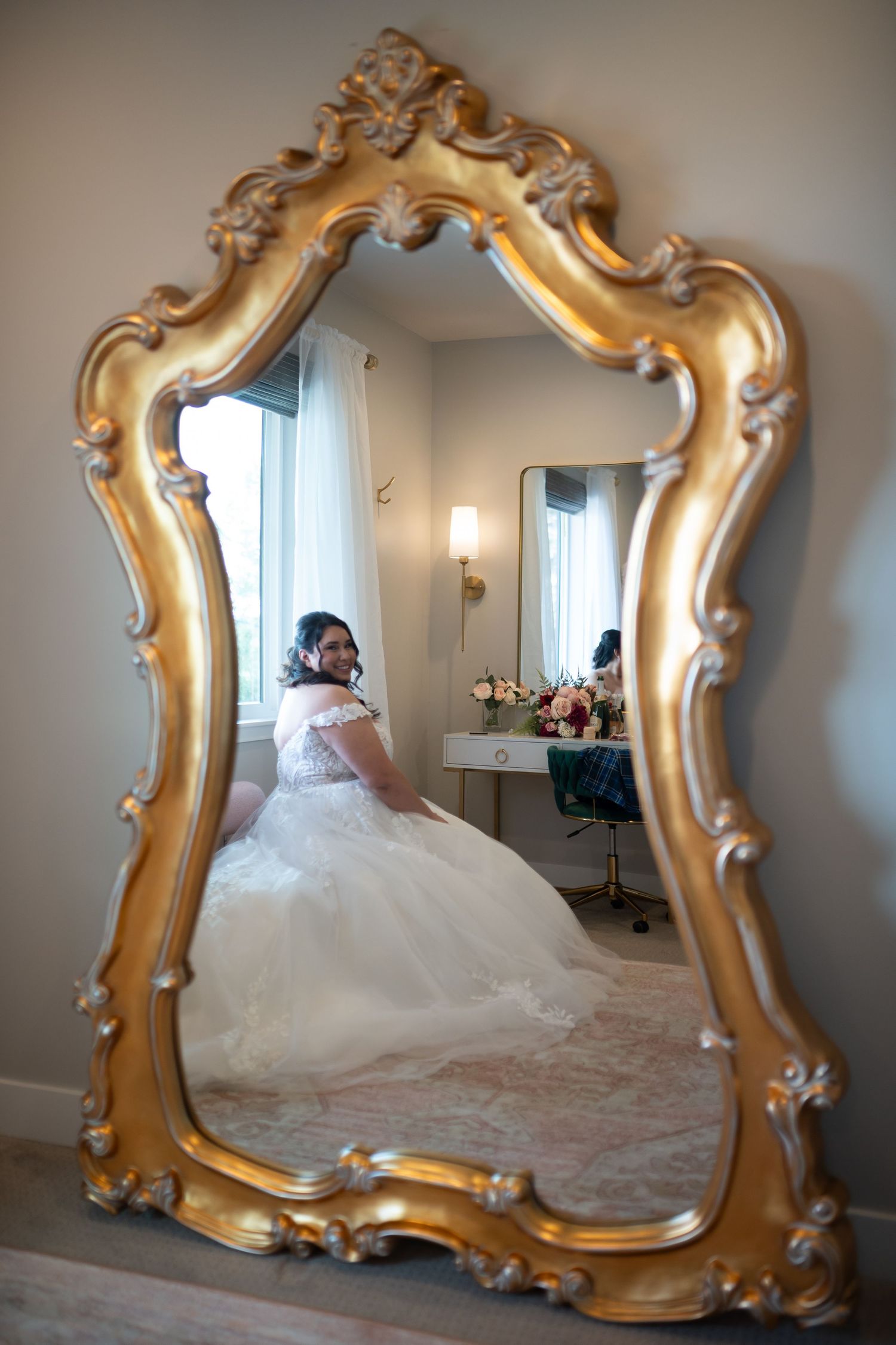 Ornate gold-framed mirror reflecting wedding dress details in a bridal fitting room.