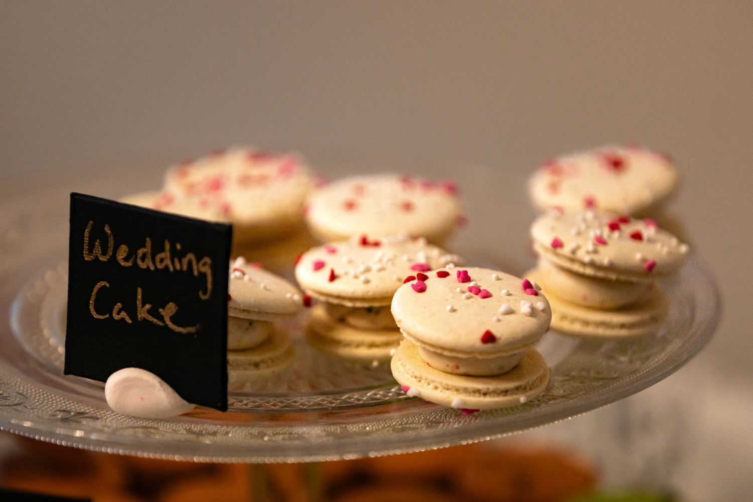 Wedding cookies with pink sprinkles displayed on a glass platter next to a small chalkboard sign.