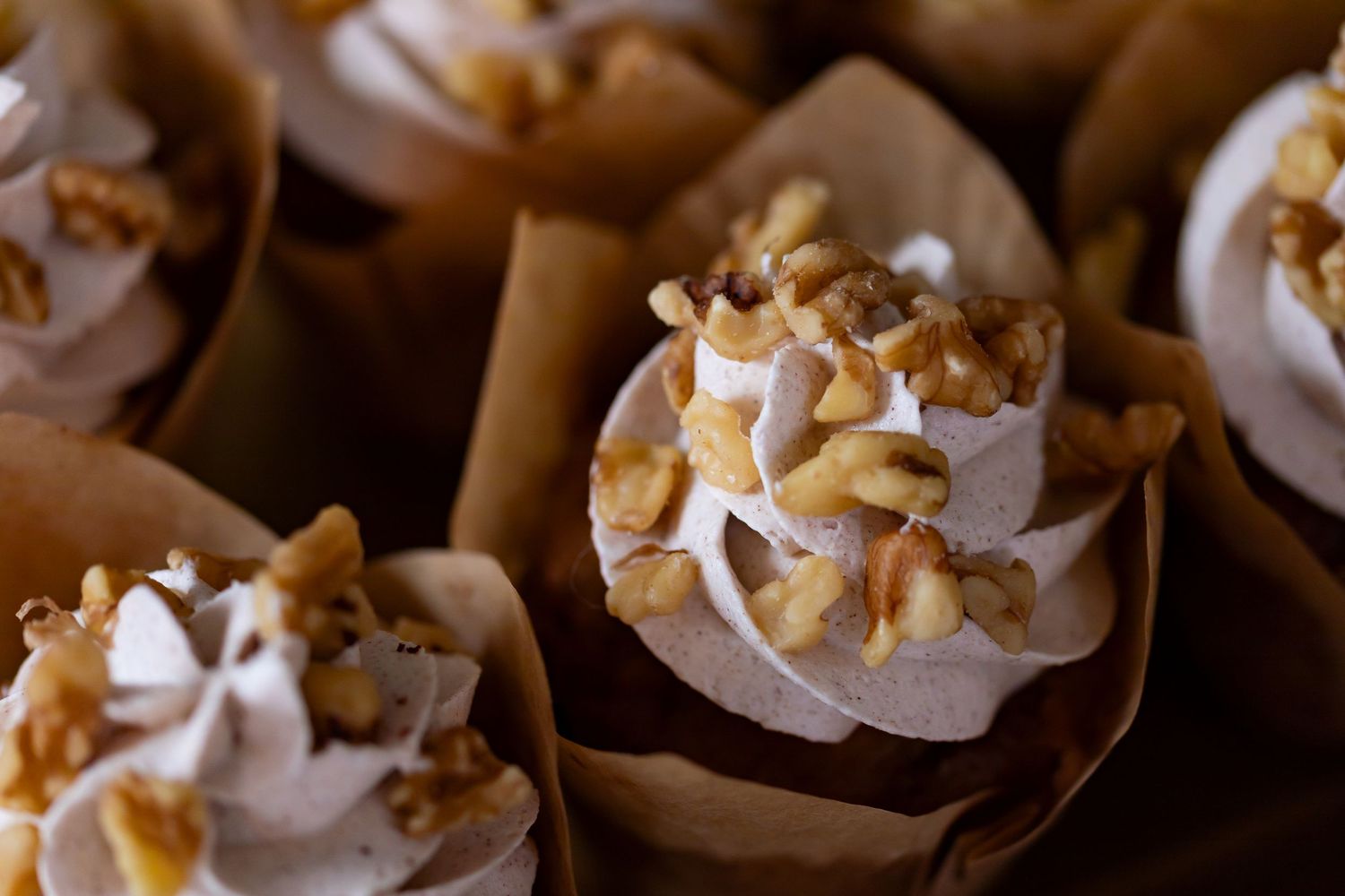 Mini dessert cupcakes topped with whipped cream and nutty garnishes in paper wrappers.