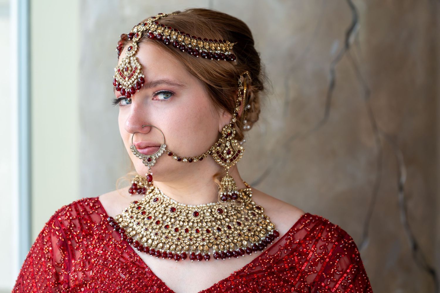 Elegant bridal portrait featuring red gown and traditional gold jewelry.