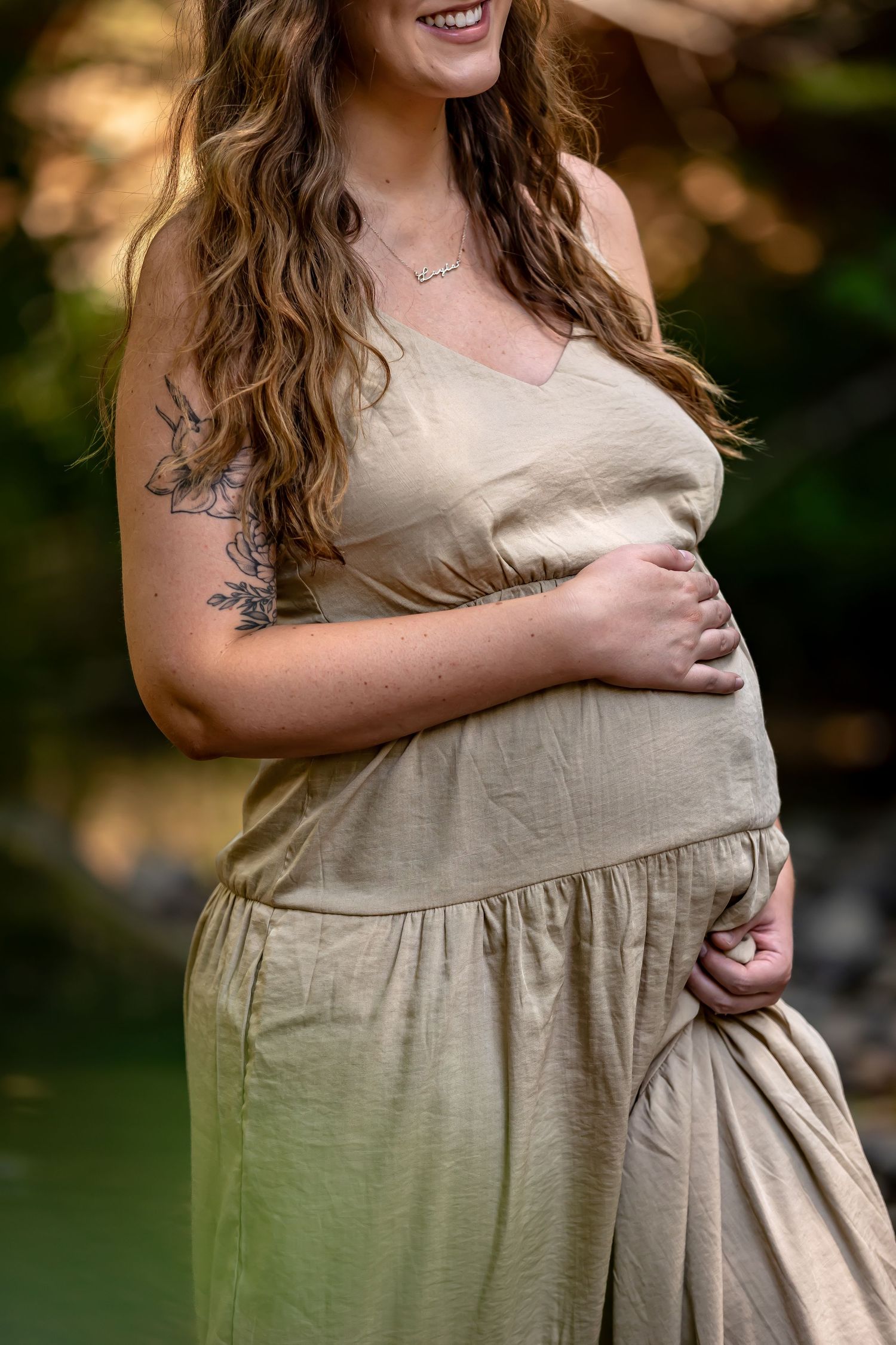 Maternity portrait in beige dress against natural outdoor backdrop.