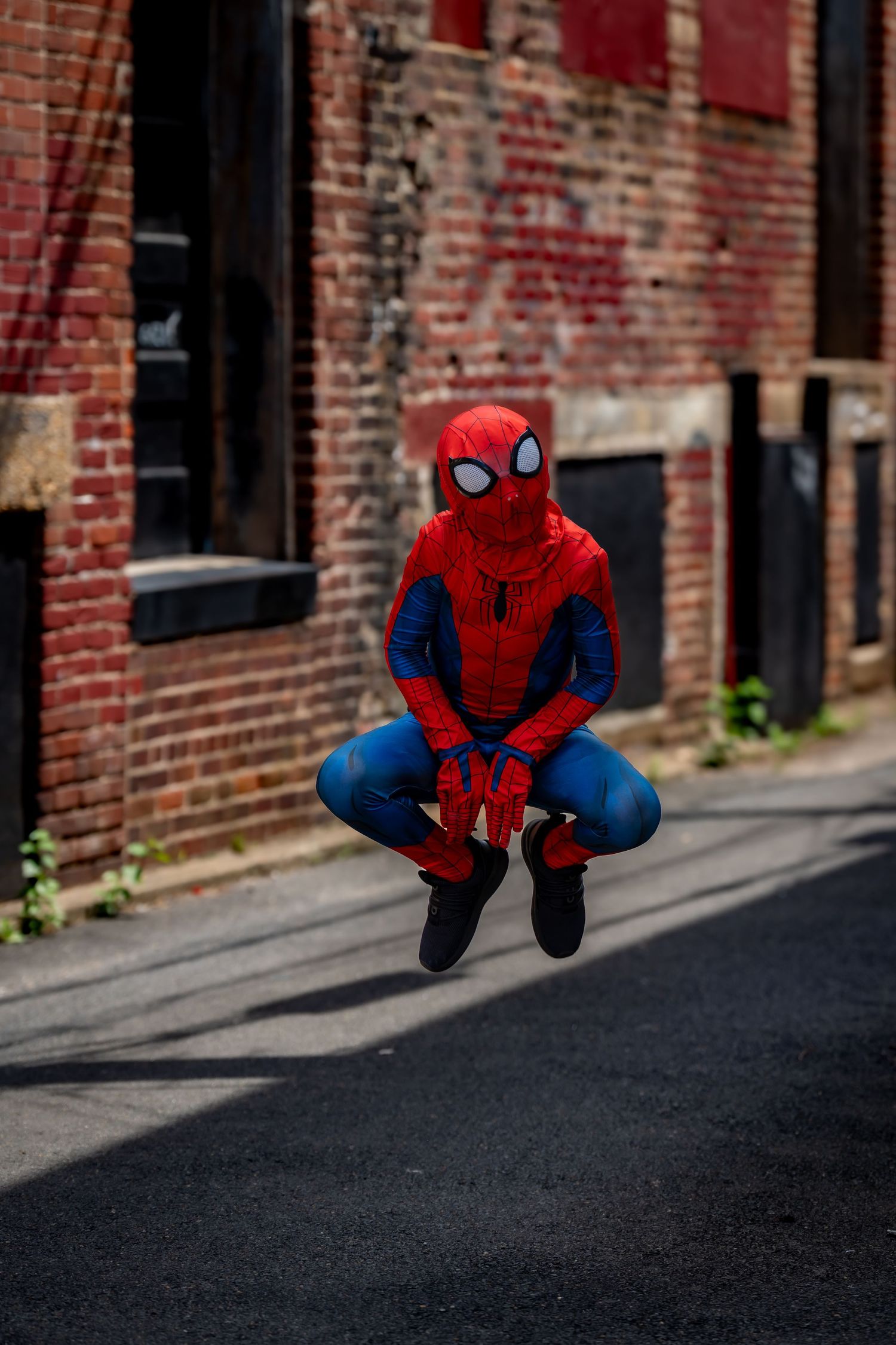 Spider-Man cosplayer demonstrating jumping poses on urban street.