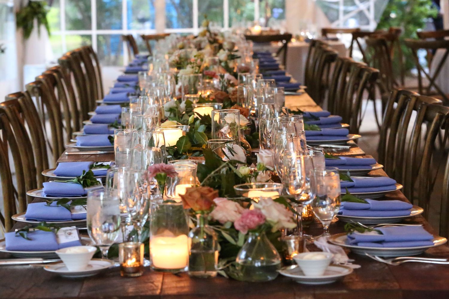 Elegant wedding table setting with blue accents, candlelight, and lush greenery centerpieces.
