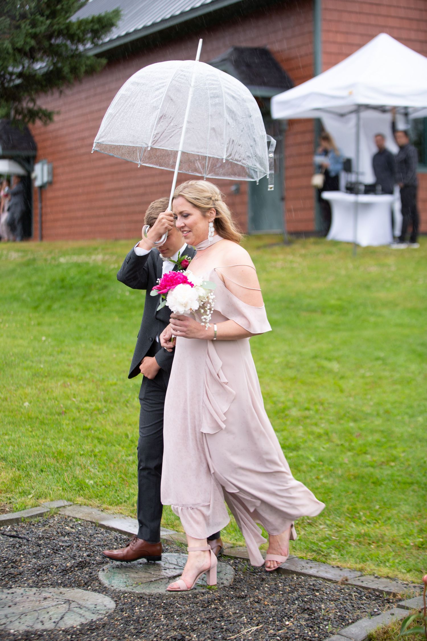 Bridesmaids in blush dresses carrying clear umbrellas during a rainy outdoor wedding.