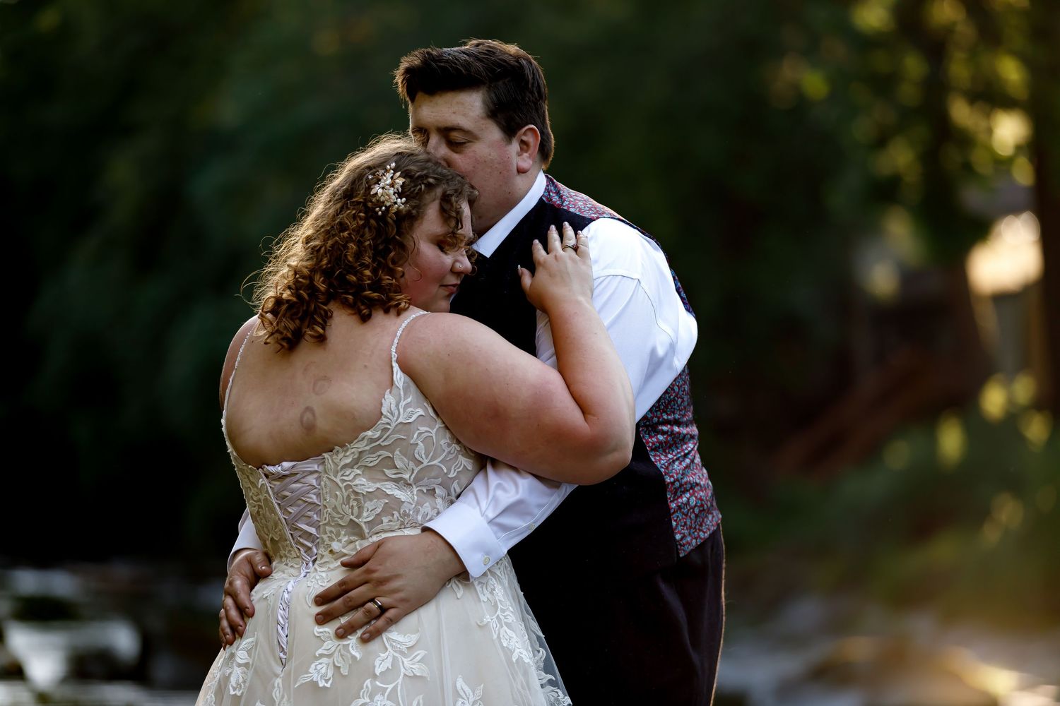 Couple embracing during romantic wedding photoshoot by river.