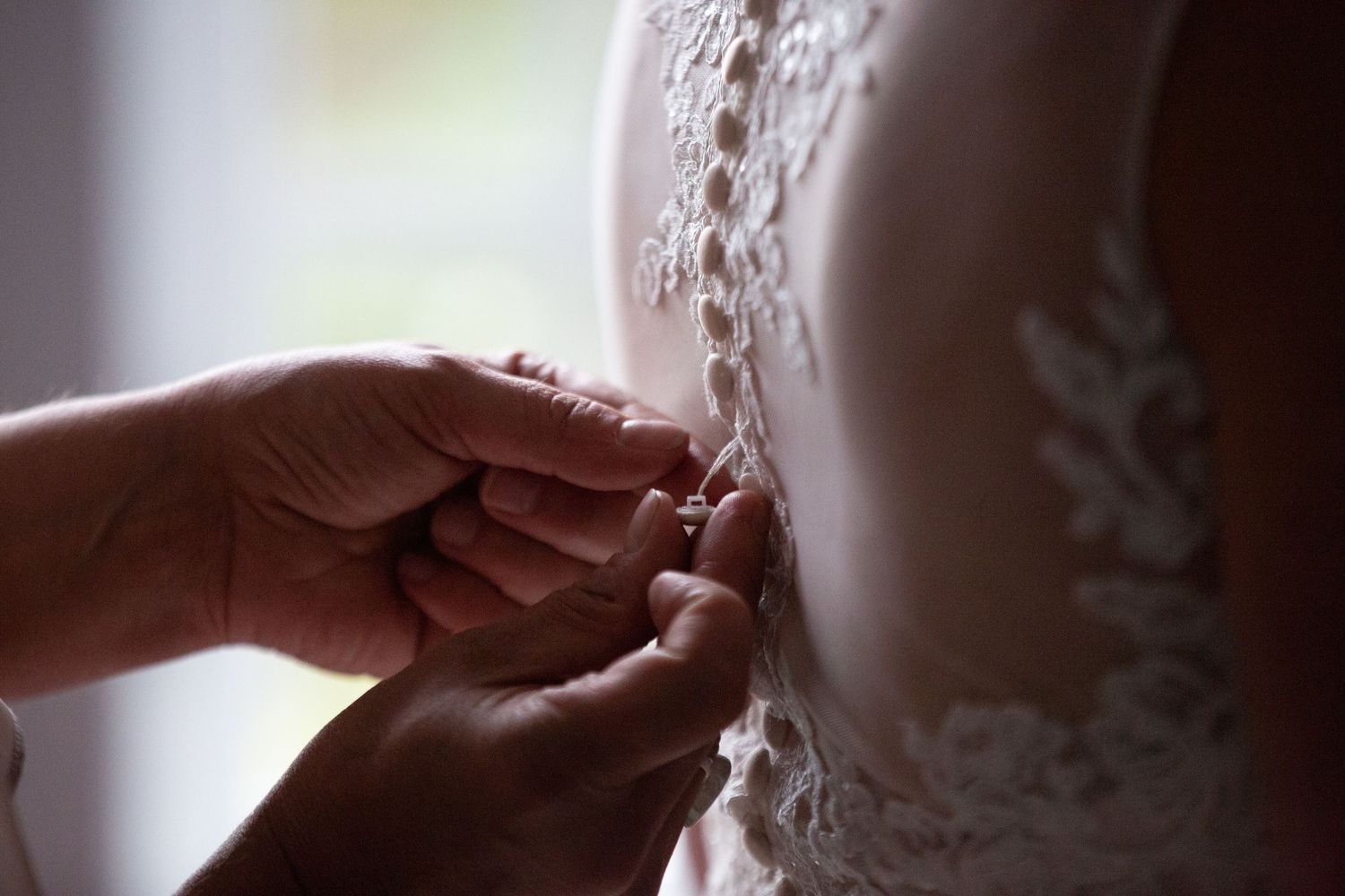 Close-up shot of hands adjusting delicate lace on a wedding dress.