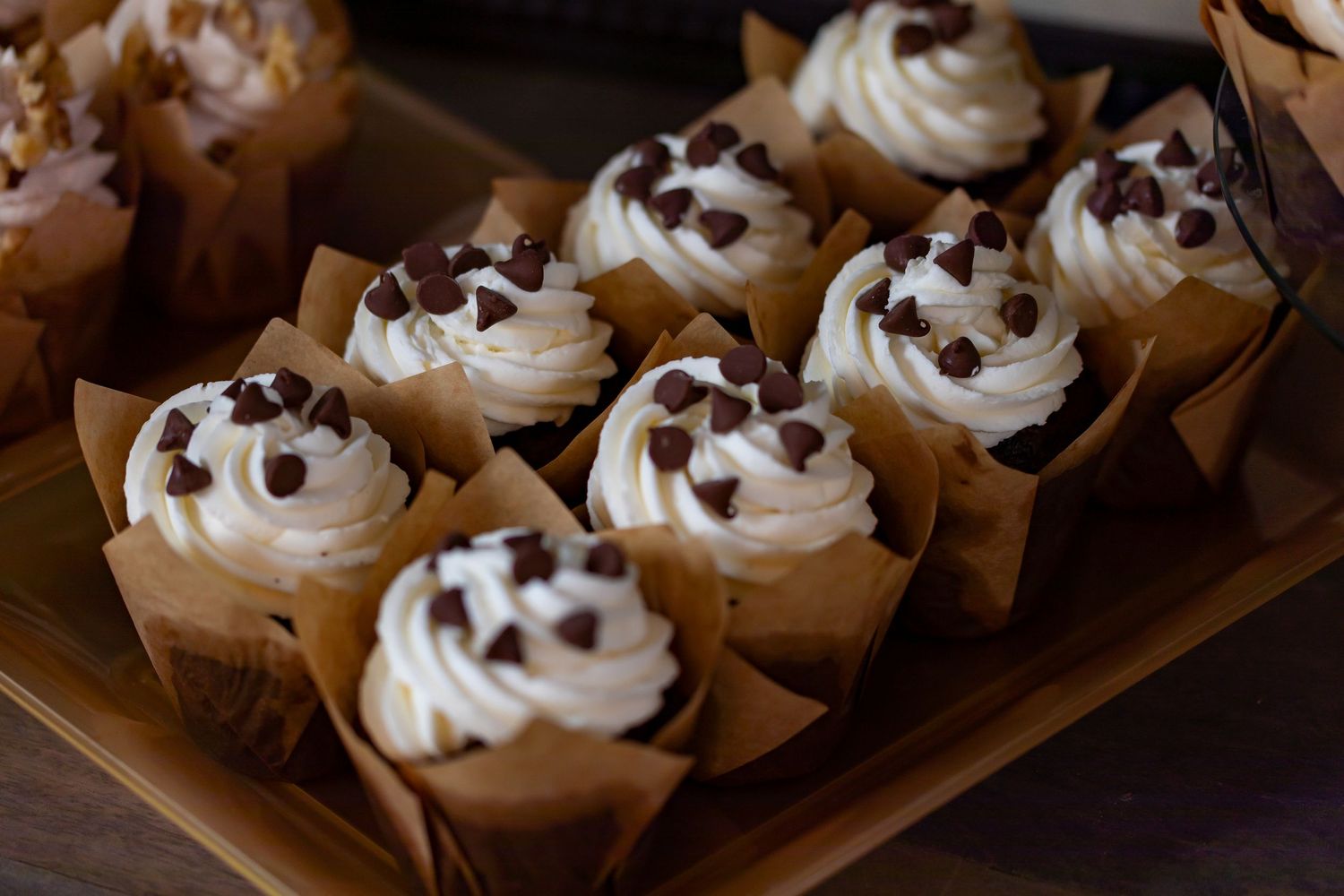 Chocolate chip cupcakes with white frosting swirls displayed in brown paper wrappers.