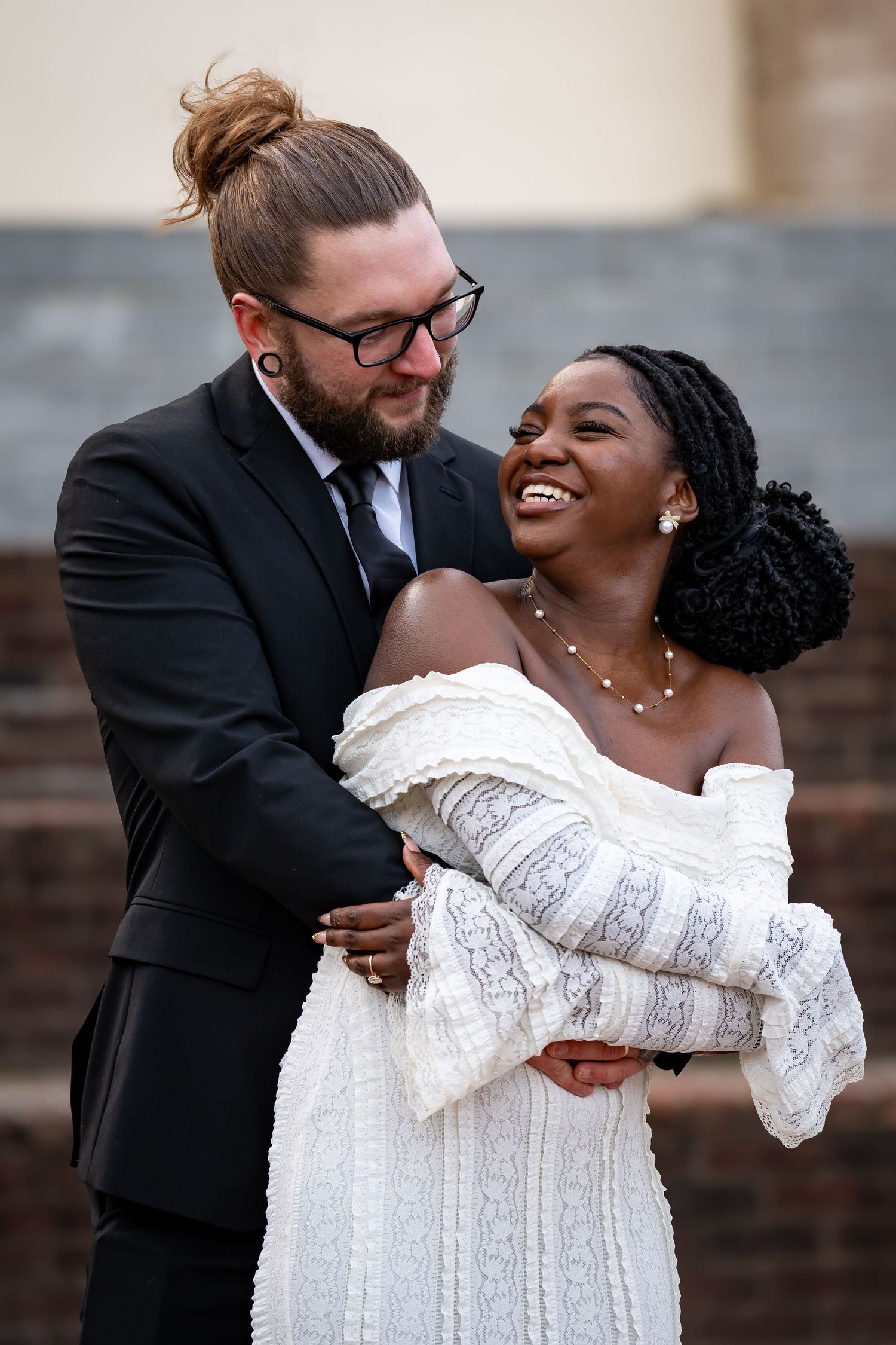 A romantic dip pose captured during a wedding photoshoot against a brick wall.
