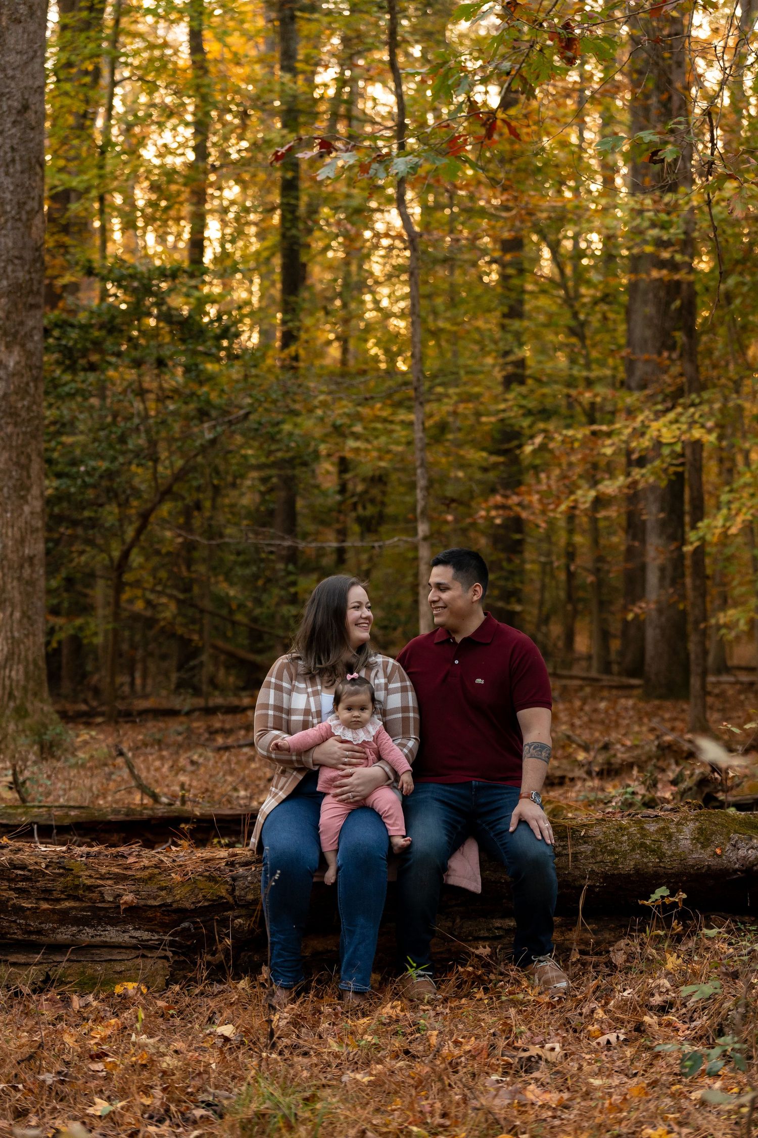 A family sitting on fallen leaves in an autumn forest setting.