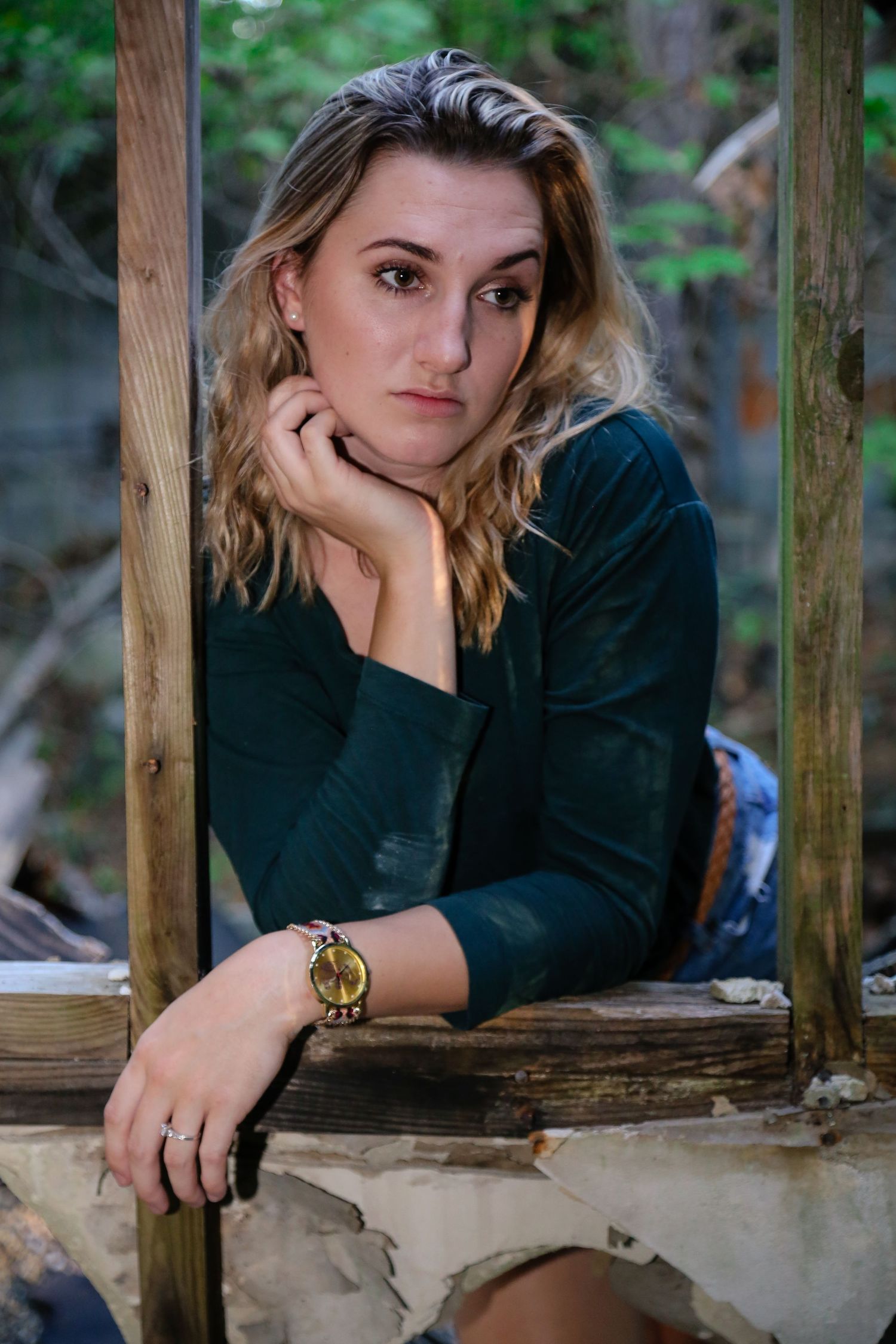 Person in black sweater resting on wooden railing in outdoor forest setting.