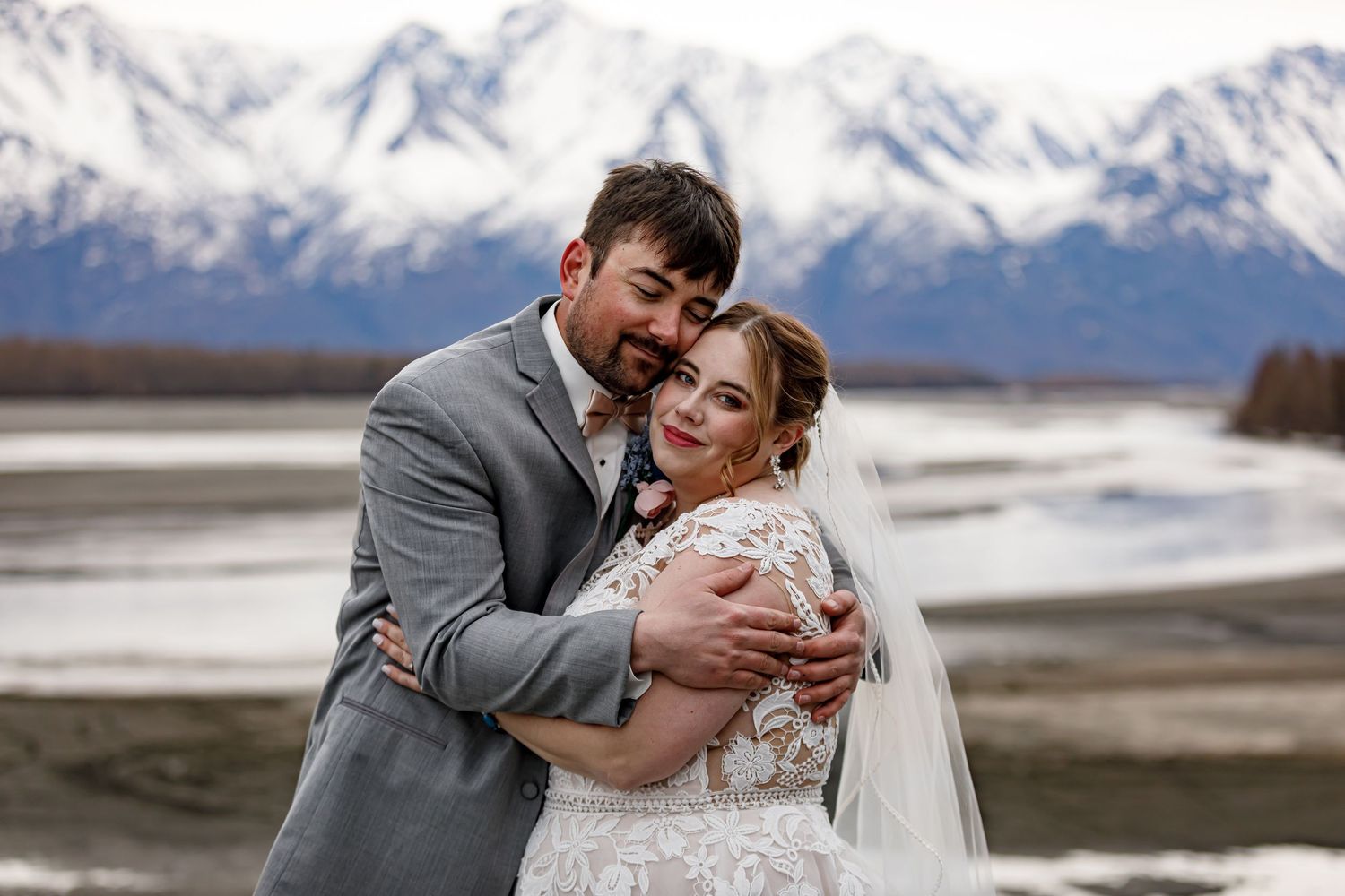 A romantic wedding couple embraces against a snowy mountain backdrop in Alaska.