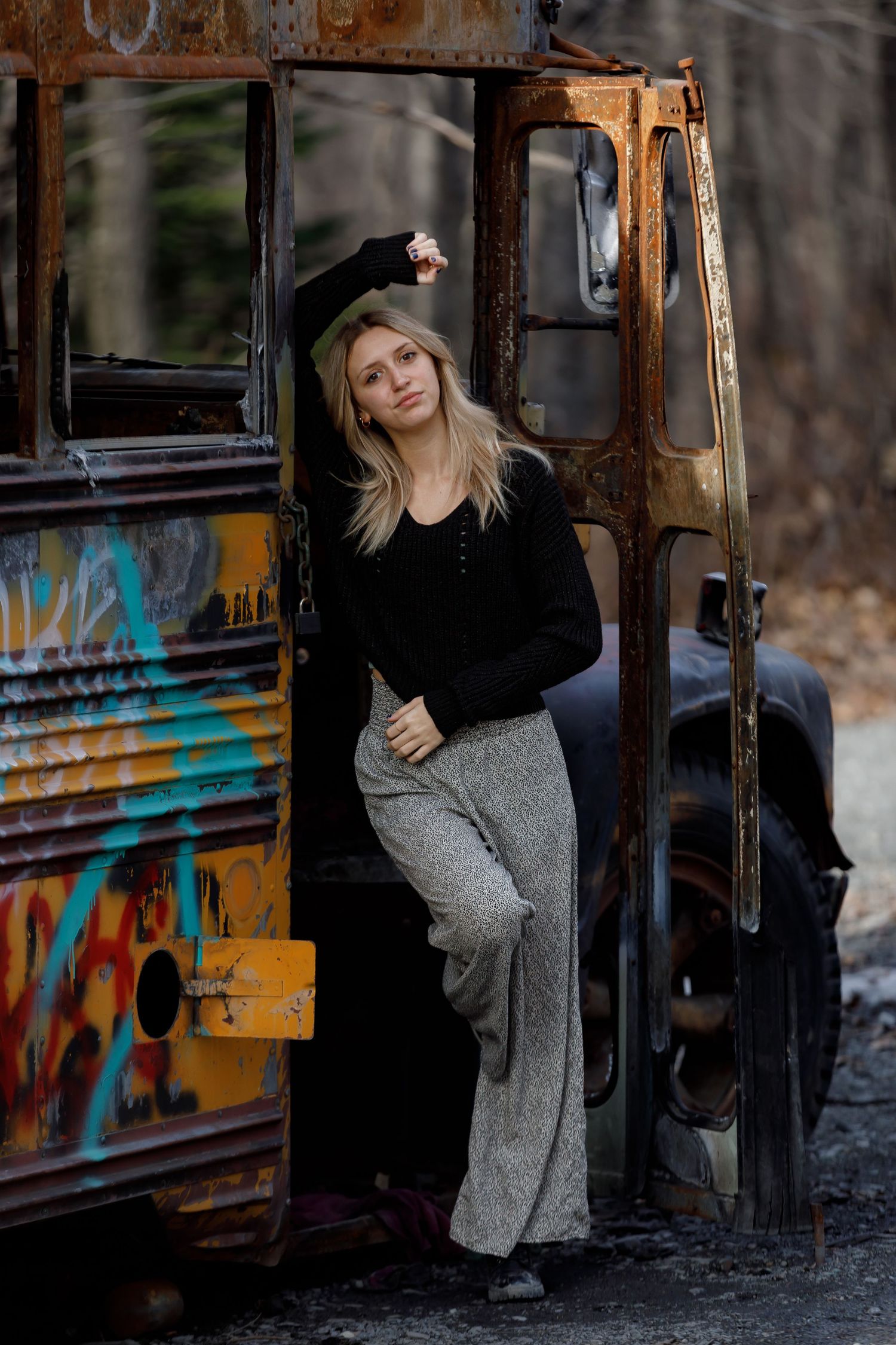 An abandoned rusty bus covered in graffiti sits in a gritty urban setting.