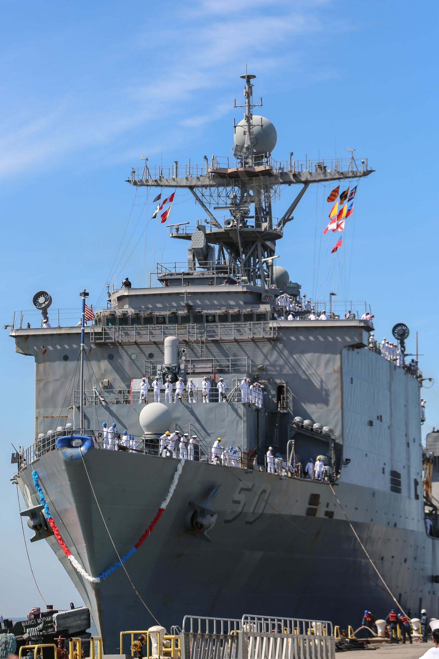 Navy warship USS Carter Hall docked with sailors manning the rails in dress whites.