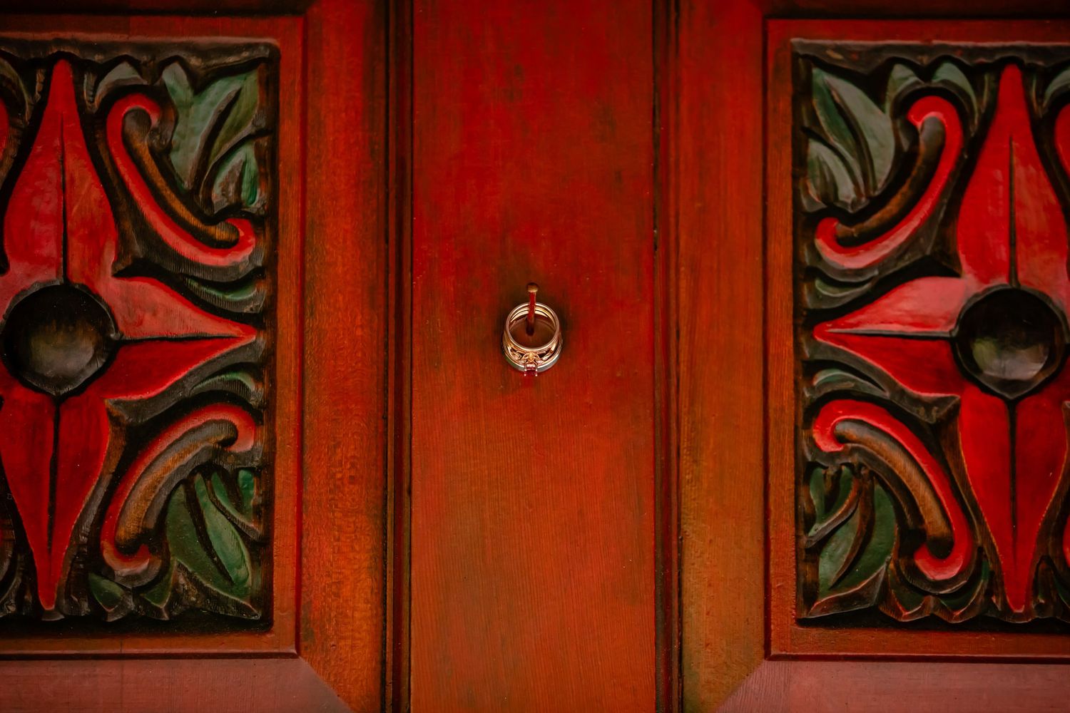 Ornate red wooden door panels with decorative floral designs and a central ring handle.