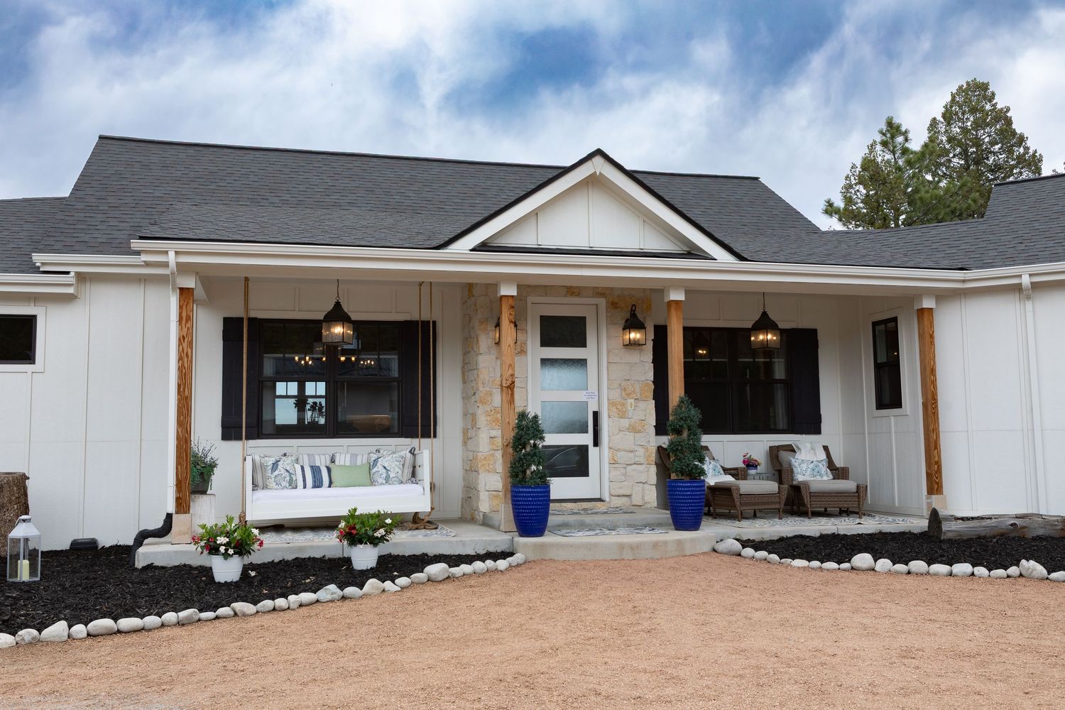 Modern farmhouse with white siding, gray roof, and covered front porch with blue accents.