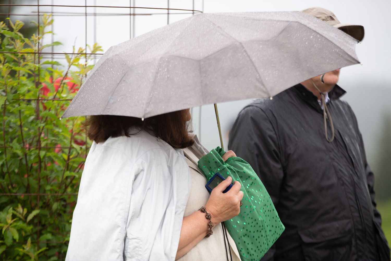 People holding white umbrellas stand together under overcast skies.