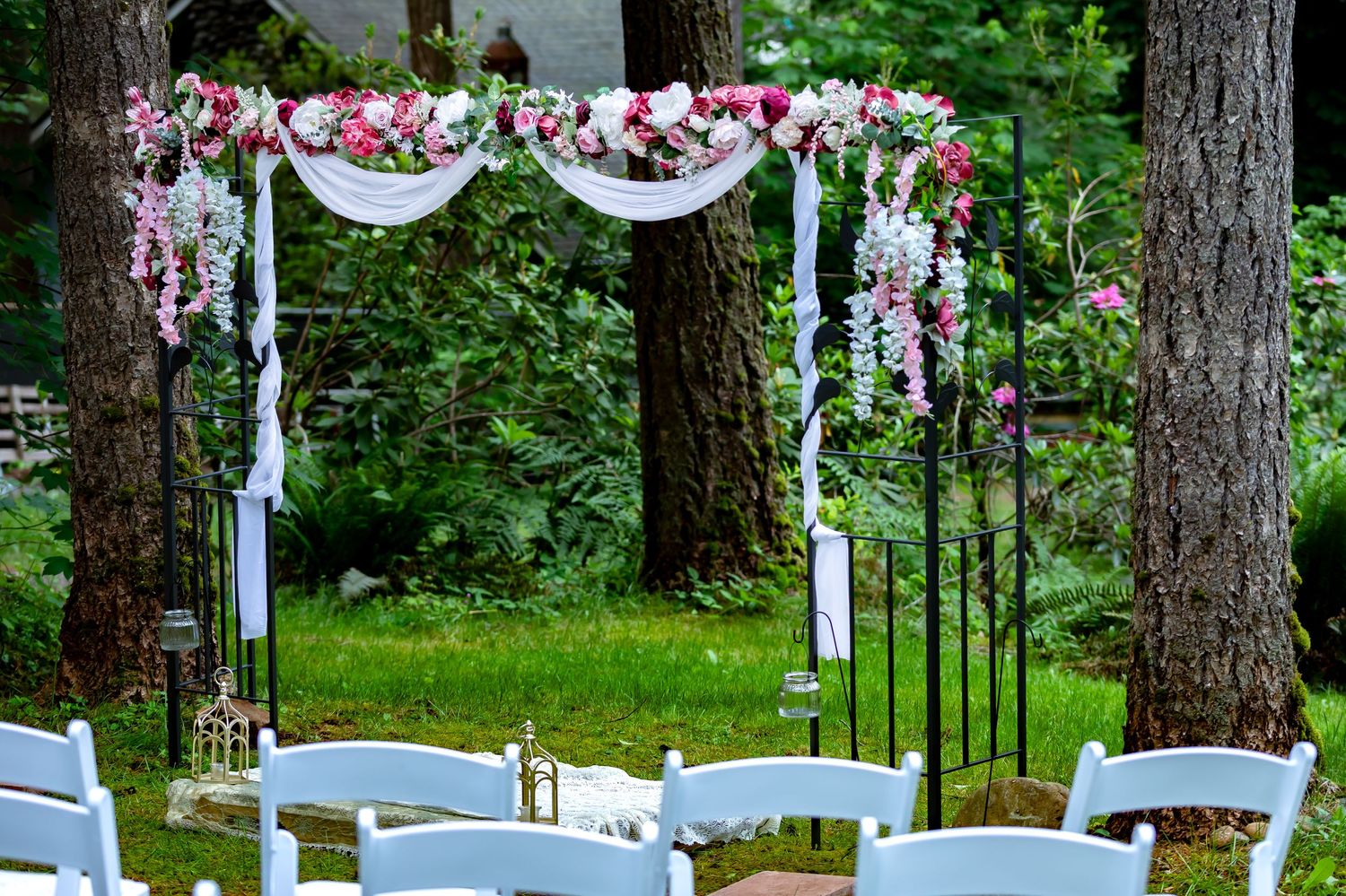 Outdoor wedding ceremony setup with white chairs and floral decorations in a pine forest.