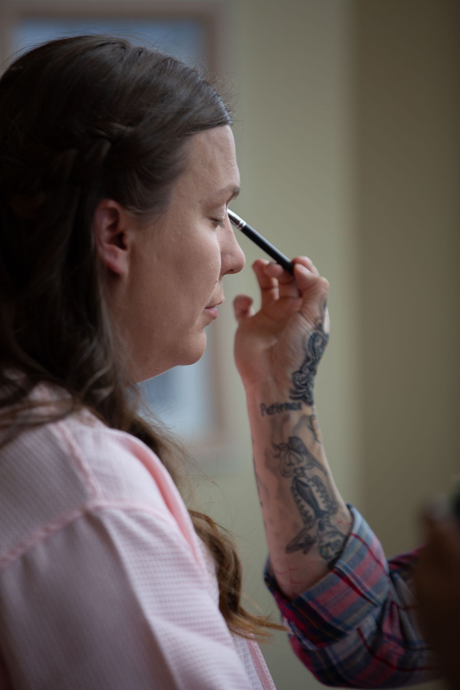 A person getting their makeup done while wearing a casual plaid shirt.