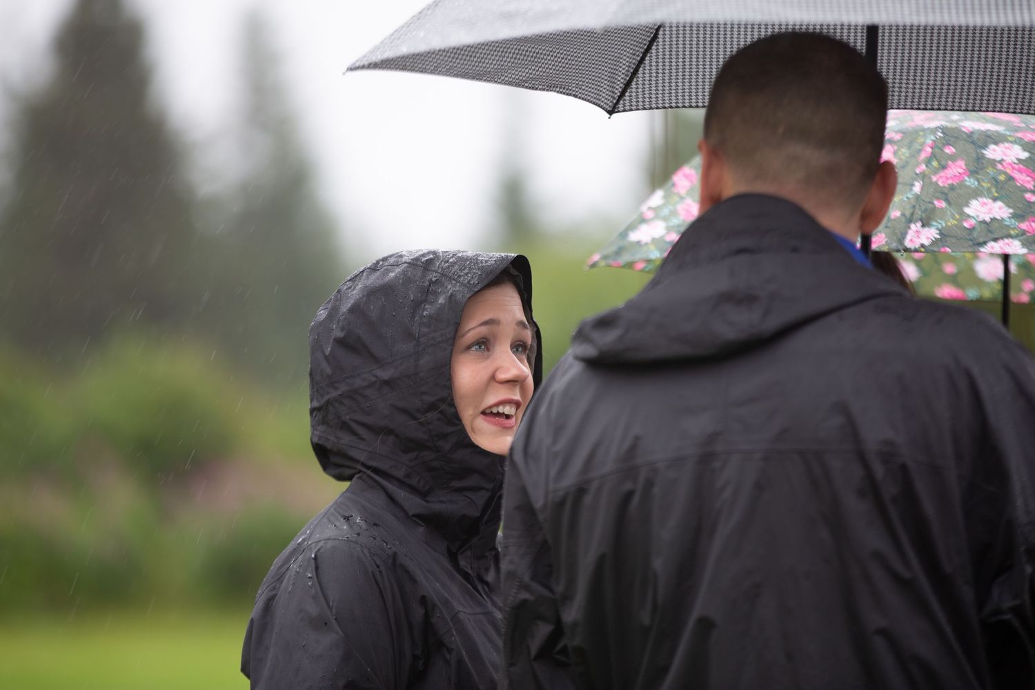 Wedding party members walking outdoors while holding black umbrellas on a rainy day.