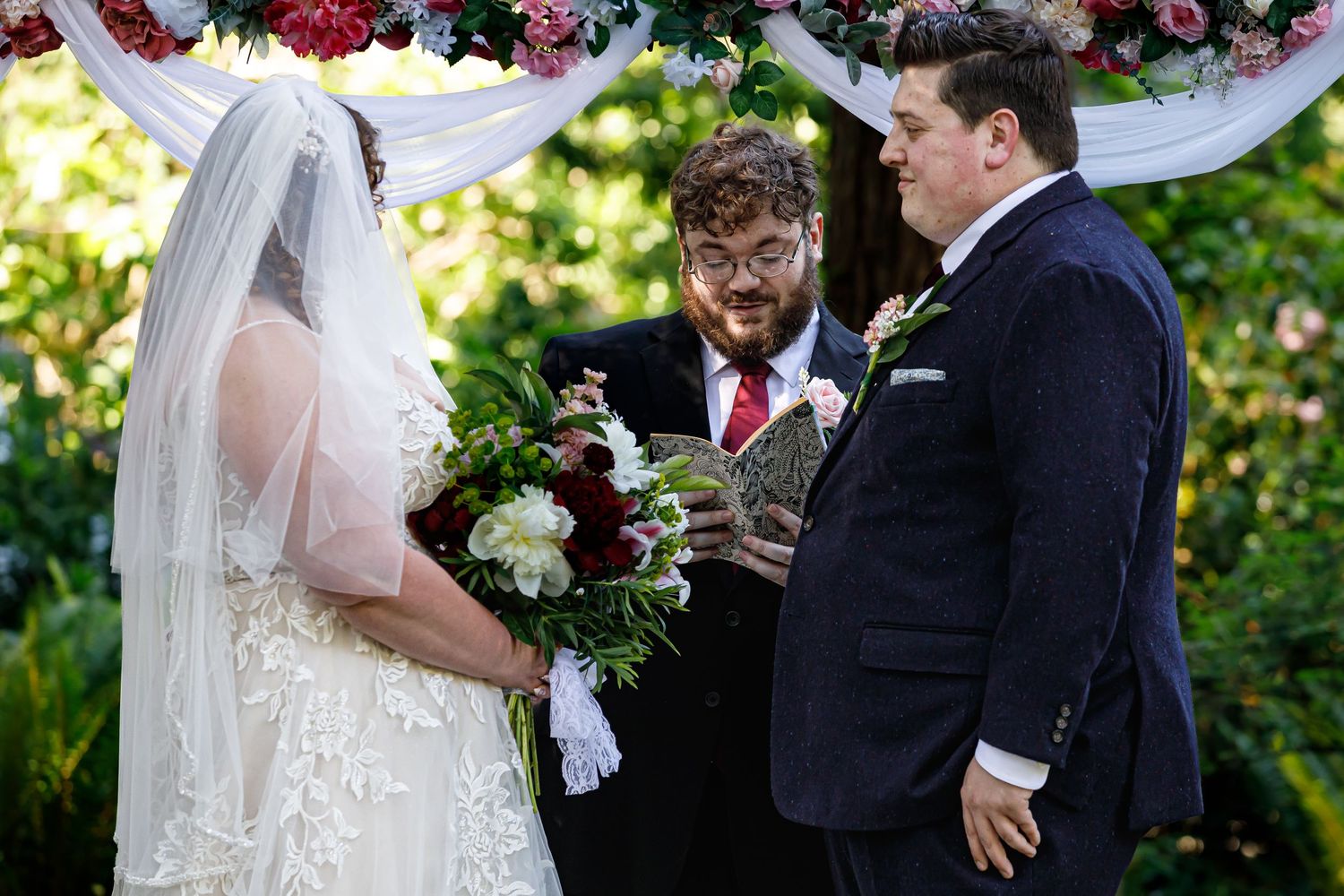 Wedding couple exchanging vows under a floral arch during an outdoor ceremony.