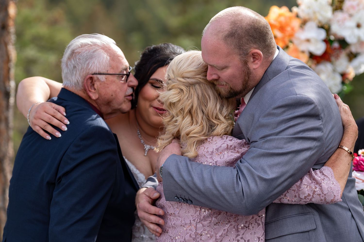 Wedding guests share warm embraces during an outdoor ceremony in a woodland setting.