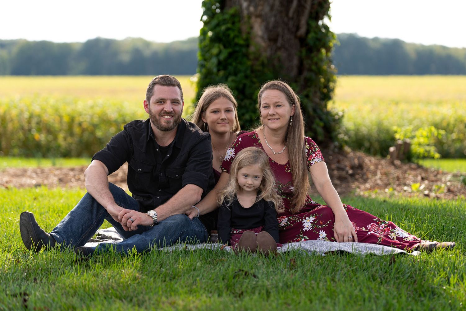 Group relaxing together on grass under large tree during golden hour photo session.