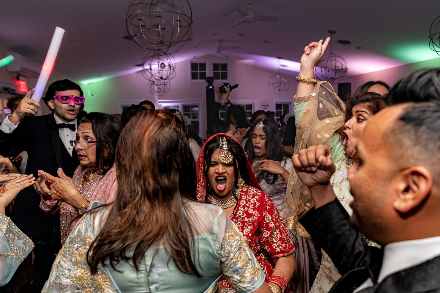 Energetic Jewish - Indian fusion wedding reception dance party with colorful lighting, glow sticks, and celebrating guests.
