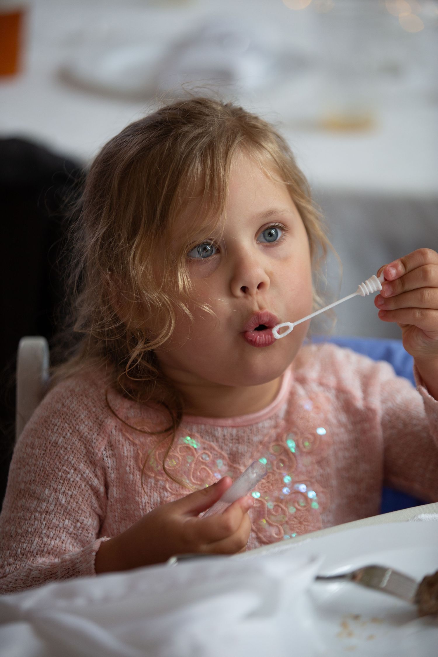 Young child in pink sweater eating with messy face at dining table.