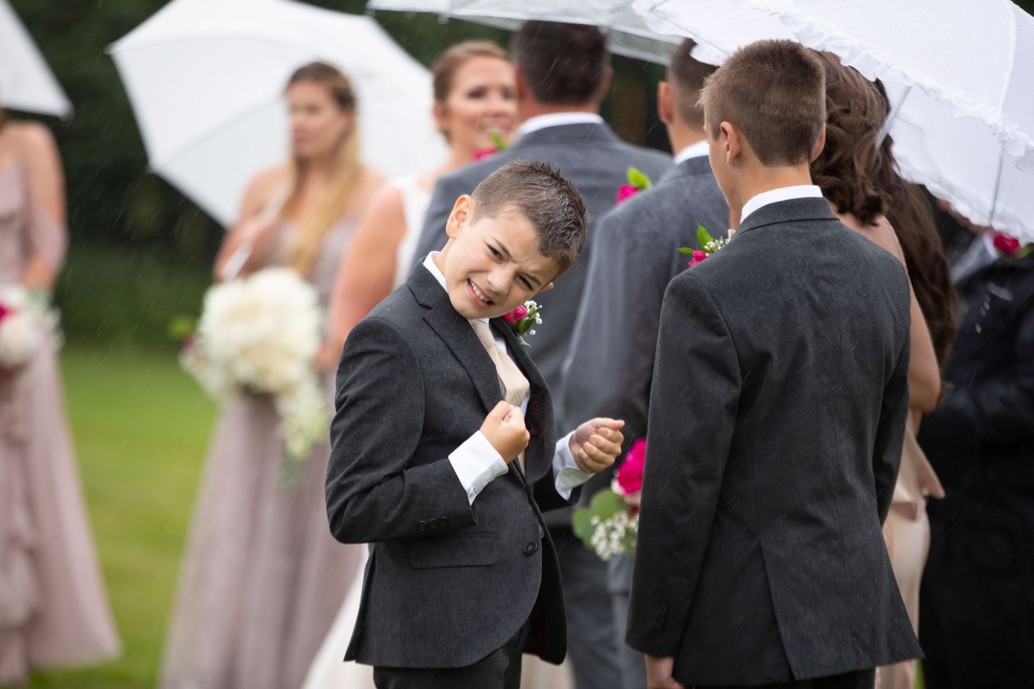 Wedding party members gather under umbrellas during a rainy outdoor ceremony.