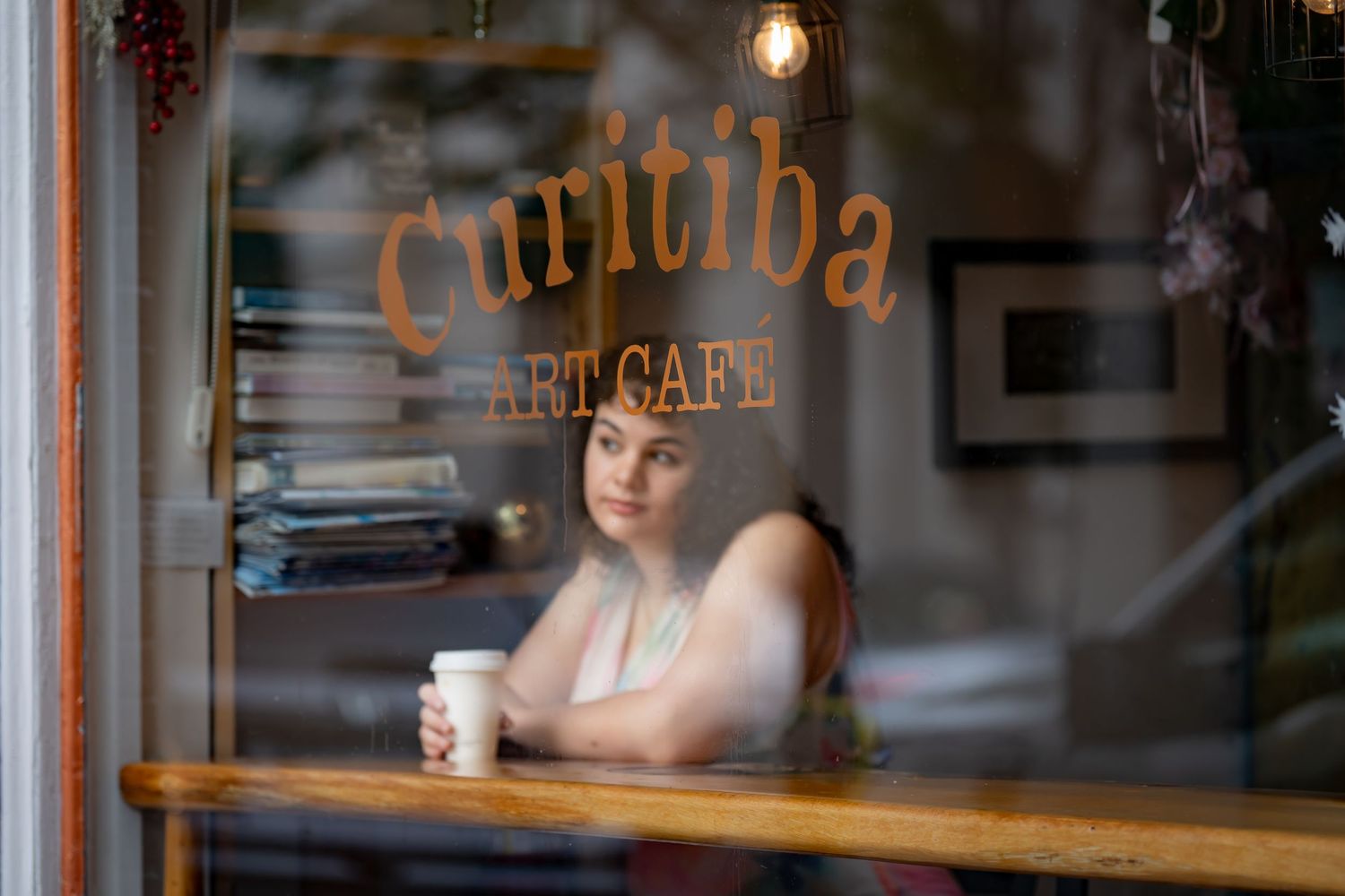 Person sits at window of Curitiba cafe with coffee cup.