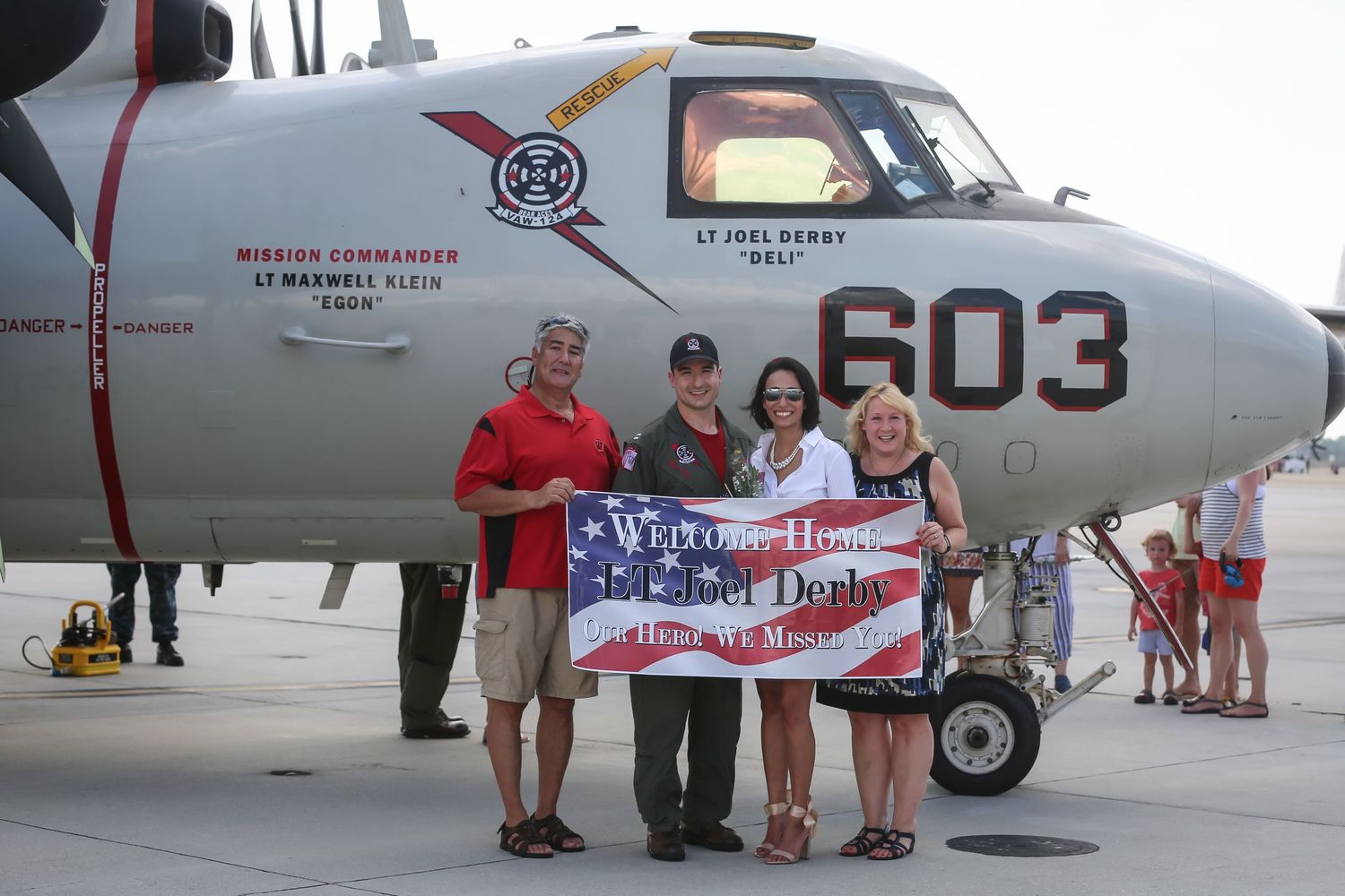 Military aircraft with welcome home banner displayed during homecoming ceremony.