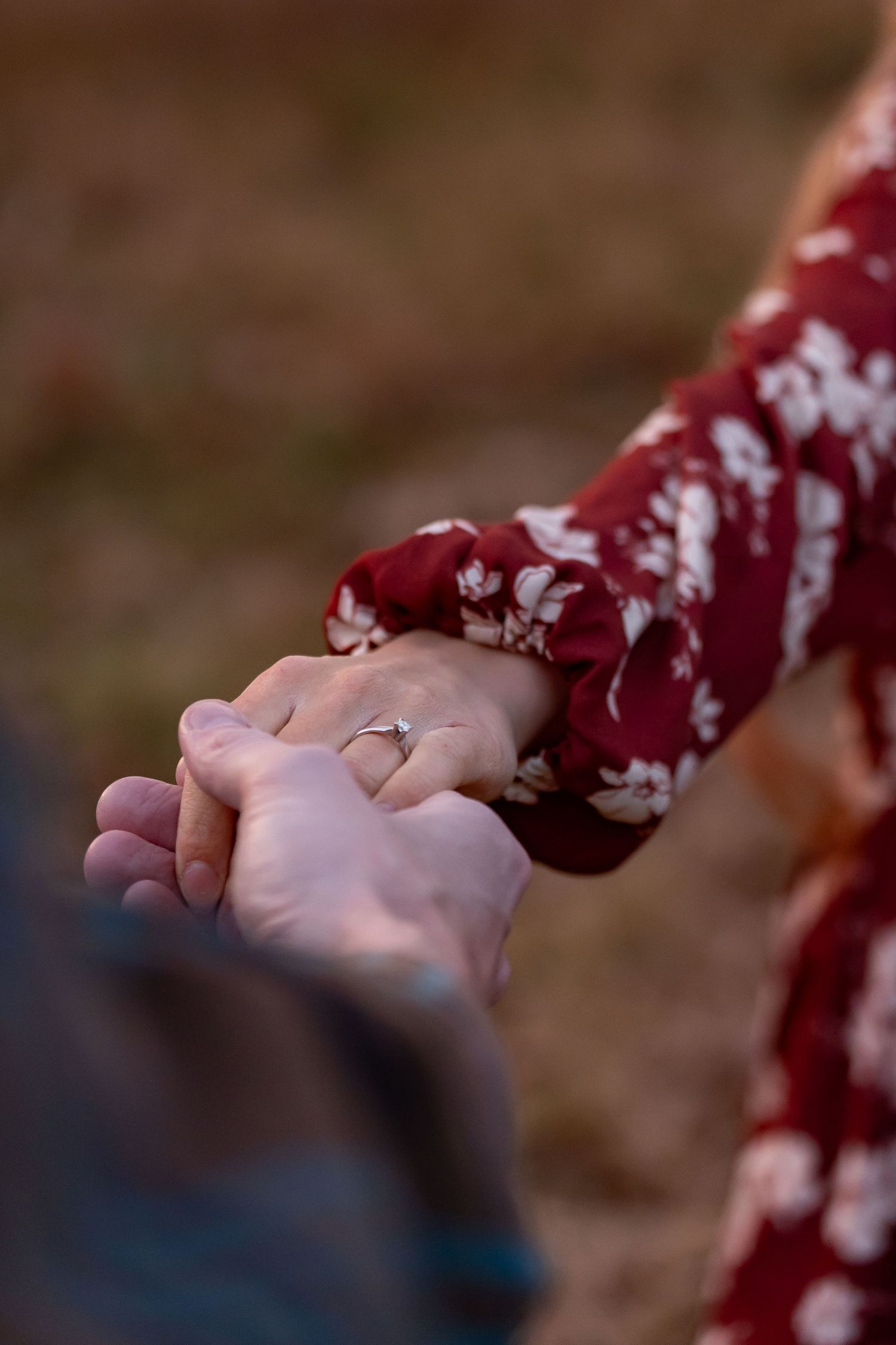 Close-up shot of hands holding with an engagement ring visible.