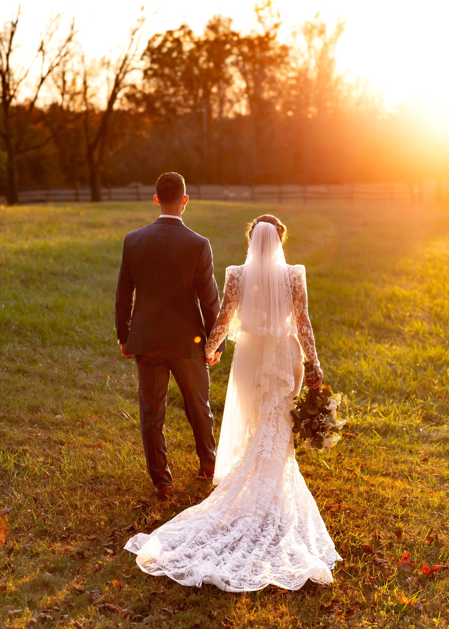 Silhouetted couple holding hands at sunset with flowing wedding dress train.